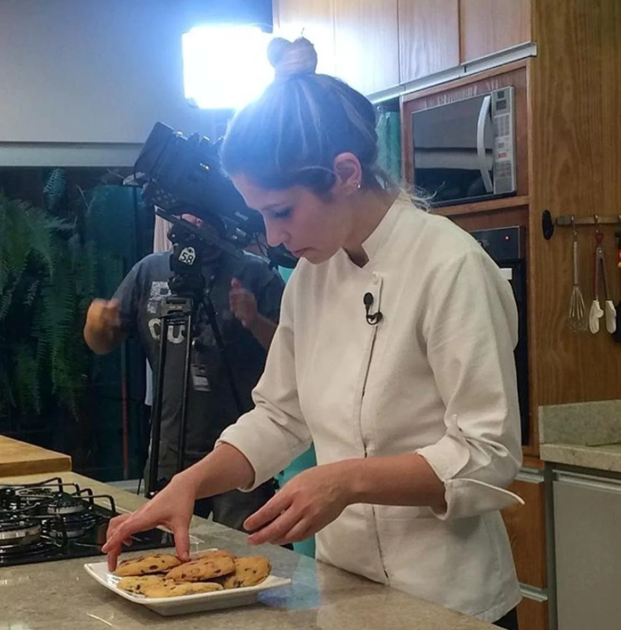 Chef arranging cookies on a plate in a kitchen, with filming equipment in the background.