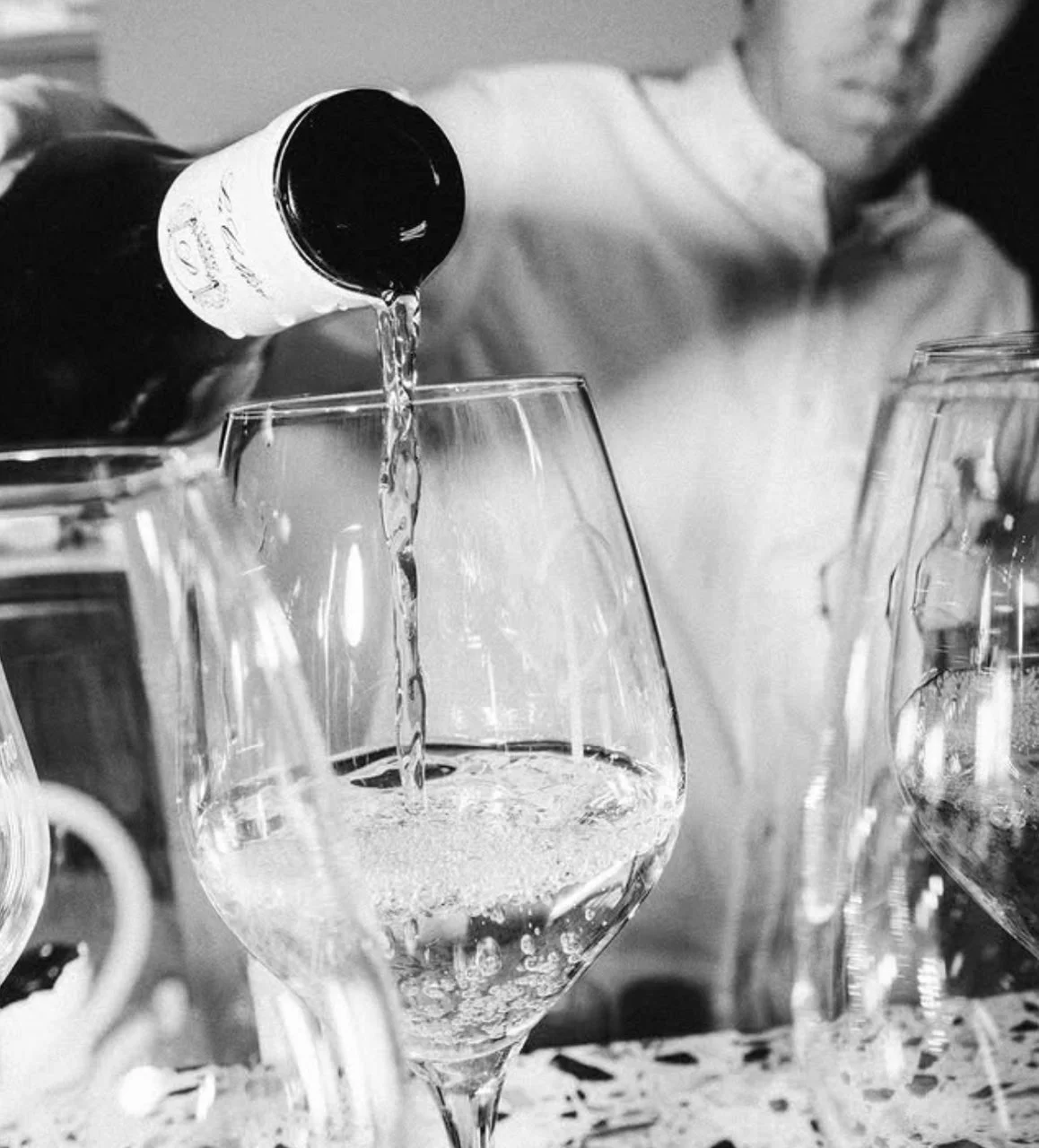 Person pouring white wine into a glass, black and white photo.