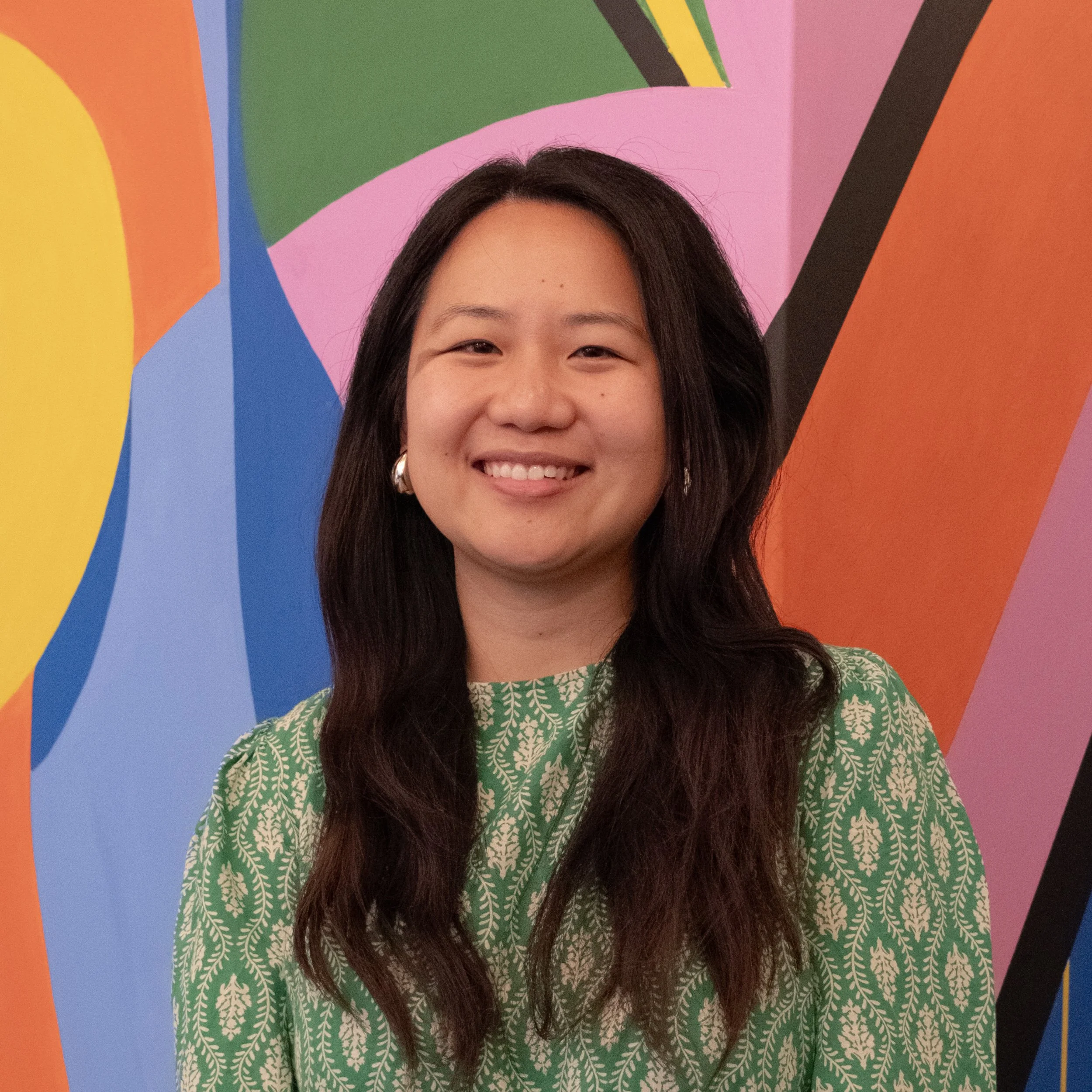 Woman smiling in front of a colorful abstract mural.