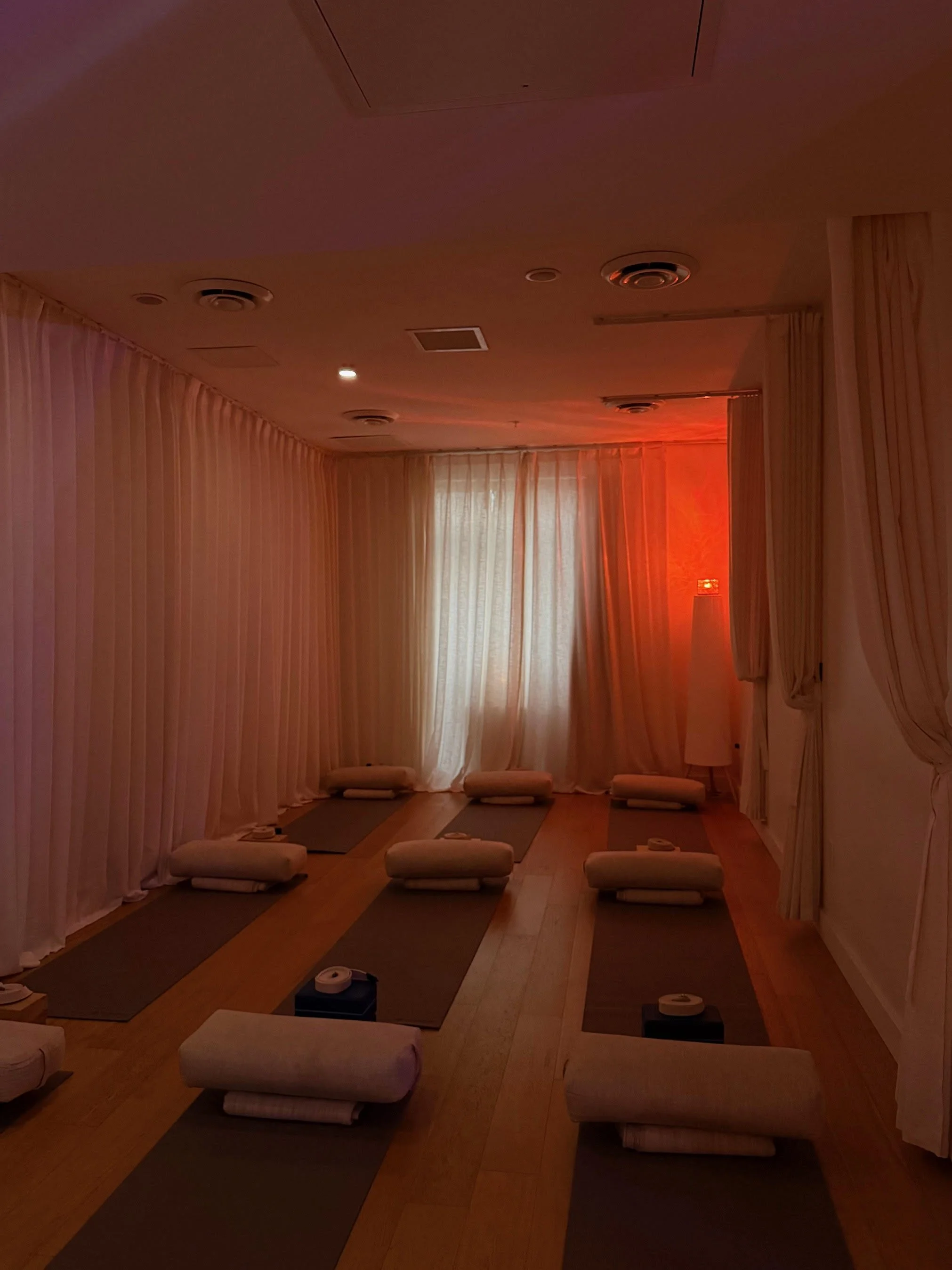 A yoga or meditation room with yoga mats, blankets, and cushions arranged on the floor, with soft lighting and curtains.