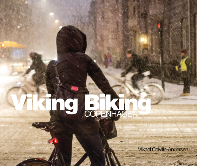A person dressed in winter clothing riding a bicycle in a snowy city street at night. Cover art for the photo book by Mikael Colville-Andersen called Viking Biking, featuring photos of Copenhagen cyclists in snowstorms.