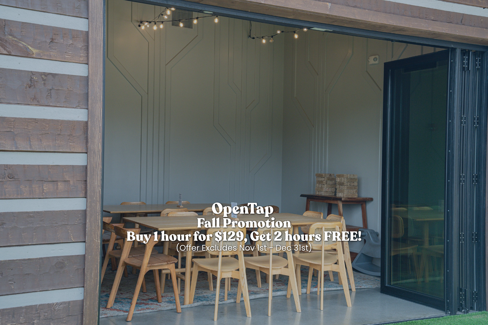 Indoor dining area with light wood tables and chairs, string lights hanging from the ceiling, brick stacks on a side table, and a sliding glass door partially open.