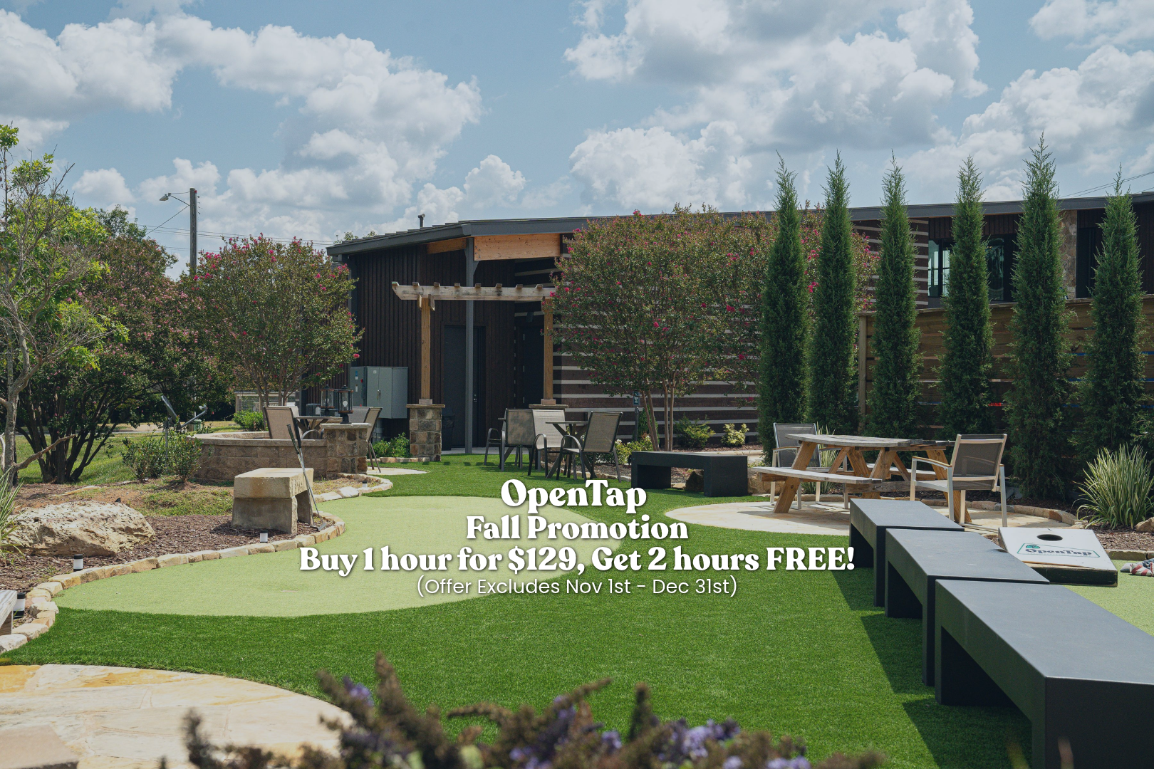 An outdoor garden with a well-manicured lawn, small trees, and outdoor furniture, with a building in the background and a partly cloudy sky.