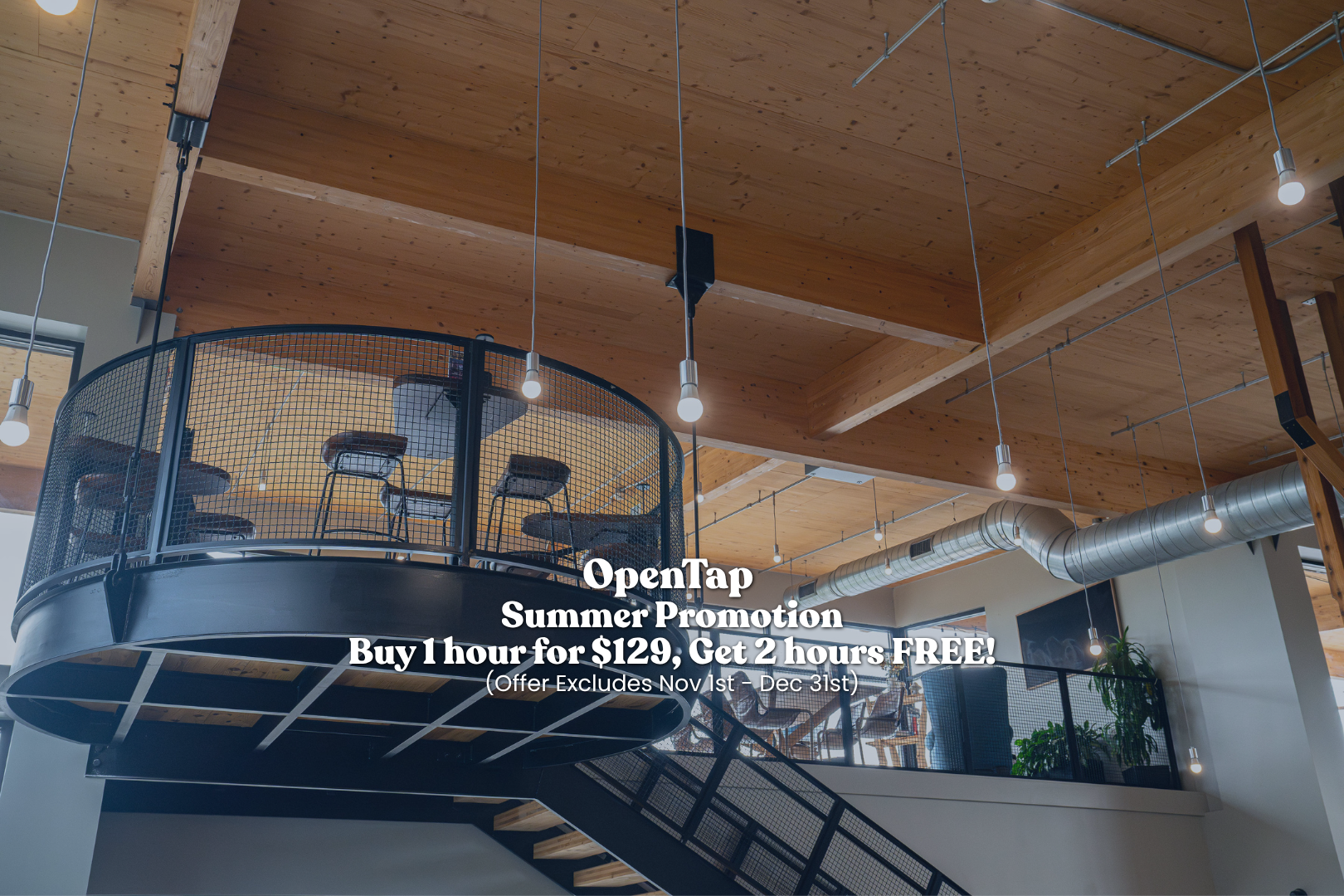 Interior view of a modern, multi-level space with wood ceilings, exposed ductwork, a circular loft with chairs, and hanging light bulbs.