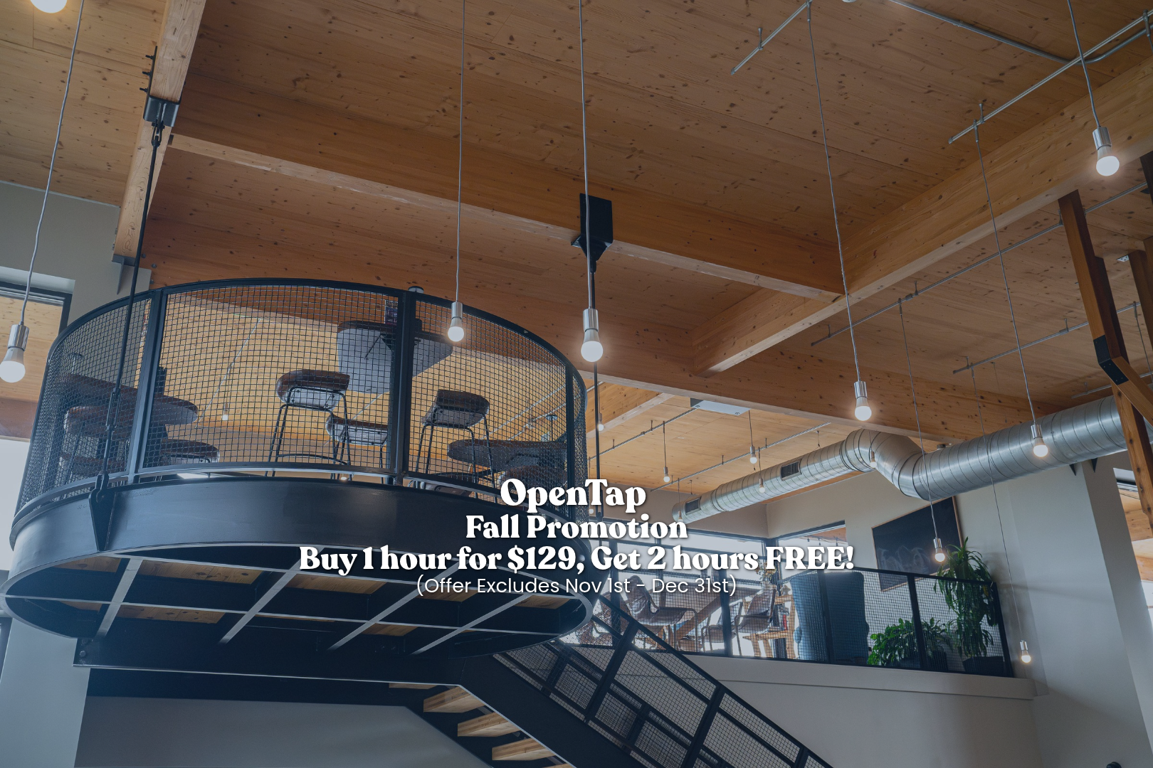 Interior view of a modern, multi-level space with wood ceilings, exposed ductwork, a circular loft with chairs, and hanging light bulbs.