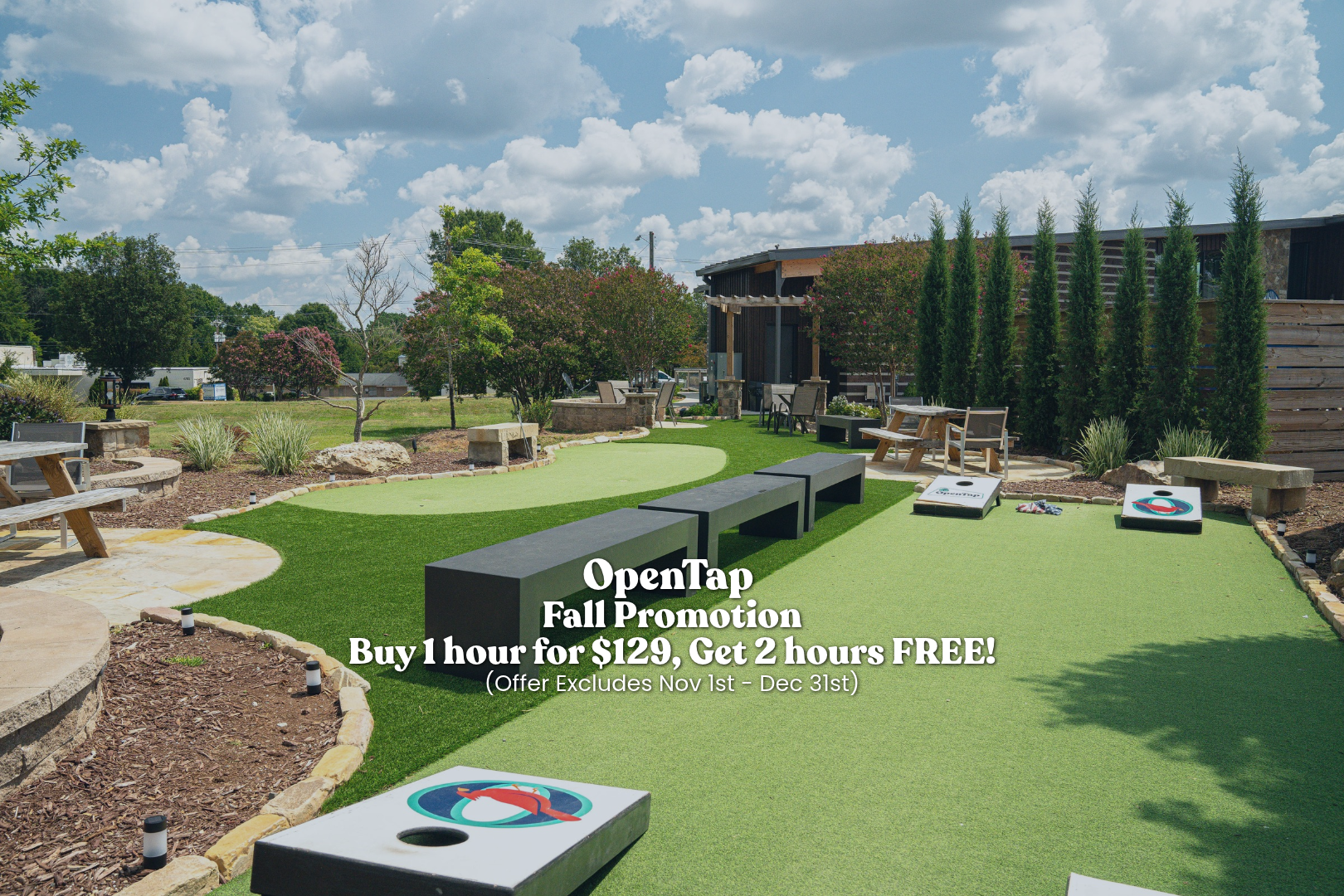 Outdoor miniature golf course with putting green, benches, trees, and cornhole boards under a partly cloudy sky.