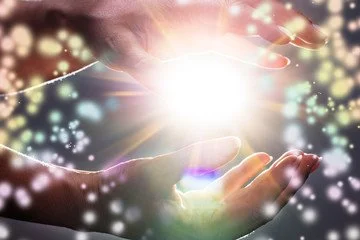 The magic of massage...hands holding bright, glowing light surrounded by colorful sparkles and bokeh effects.