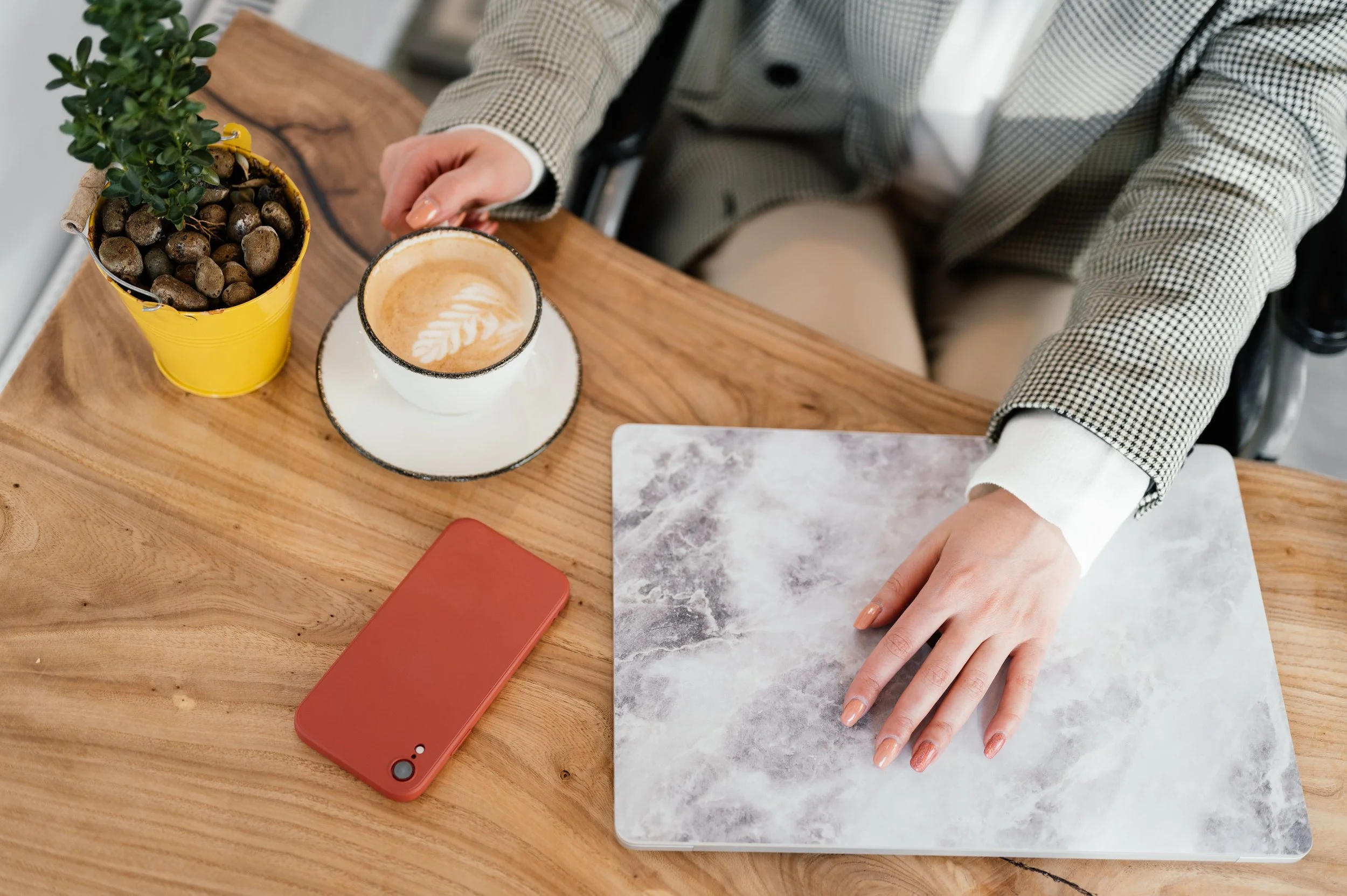 A woman's hands resting on a closed laptop at a sunlit wooden table with a mug nearby