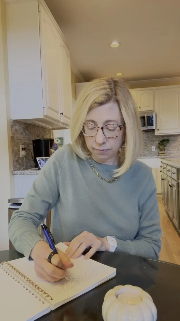 Dr. Emily writing in a spiral journal at her kitchen counter, with a white pumpkin candle in the foreground.