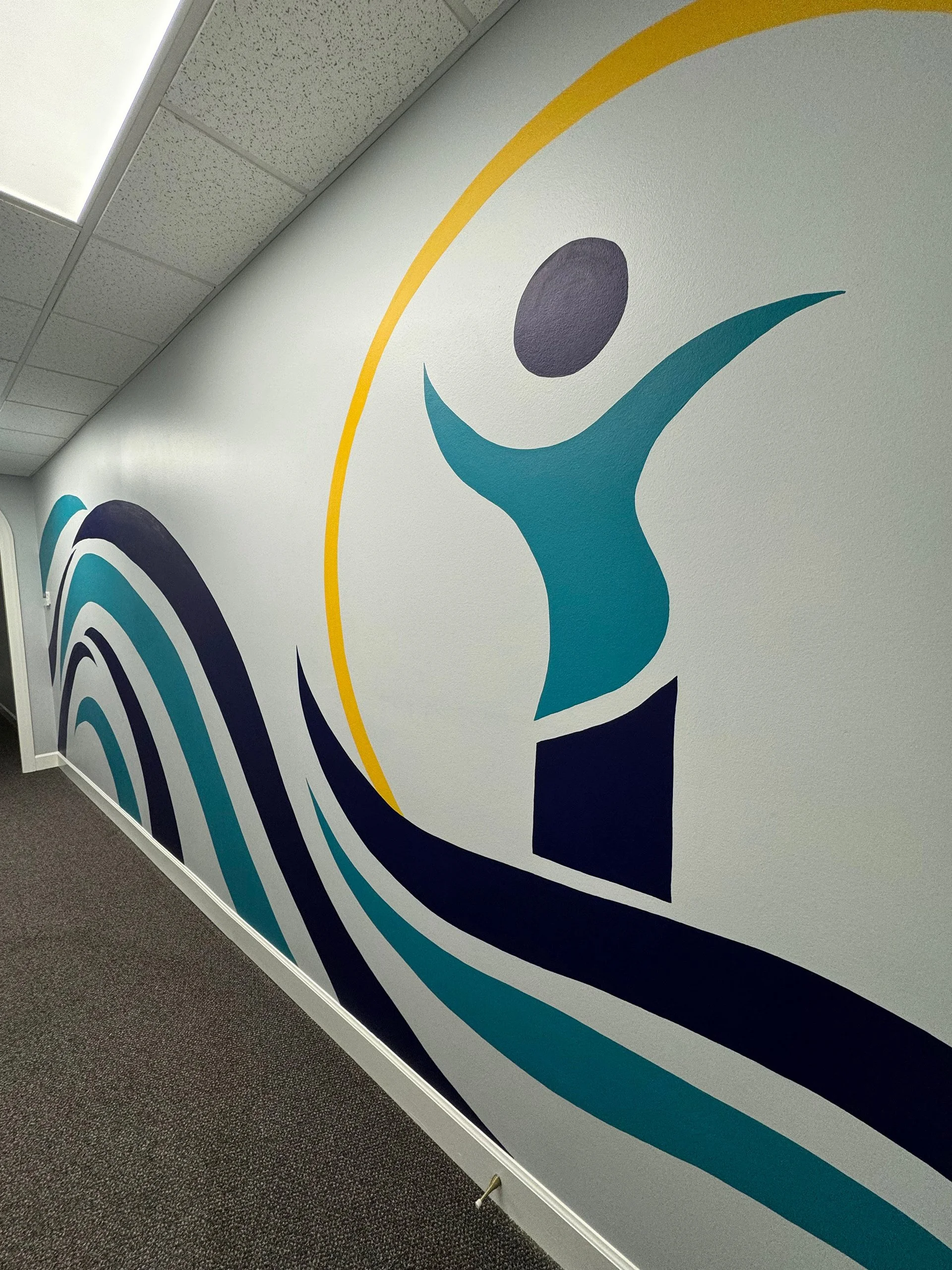 A mural on a wall featuring a stylized human figure with arms raised, surrounded by concentric arcs in shades of blue, black, and yellow.
