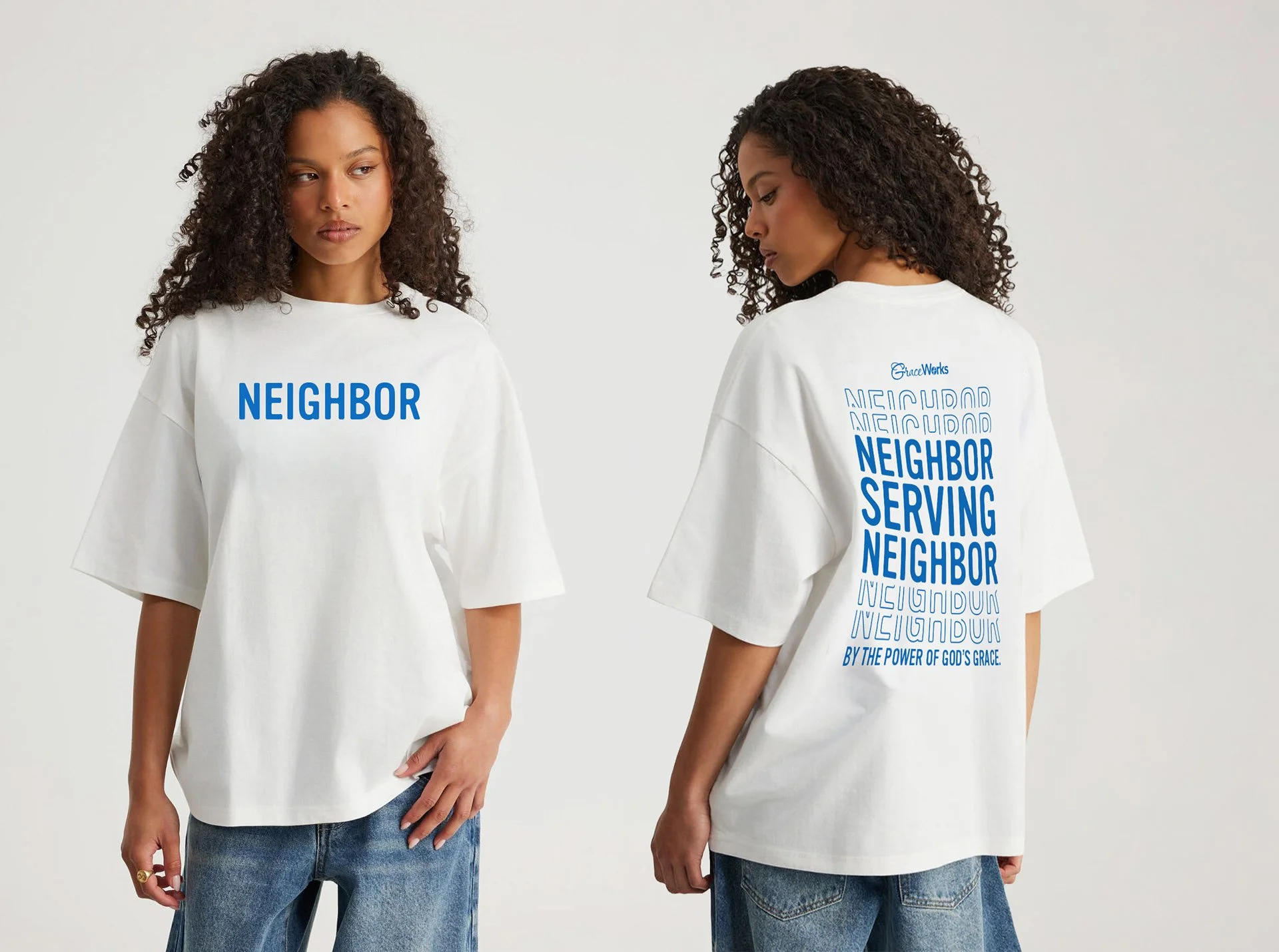 Two women with curly hair wearing oversized white T-shirts and blue jeans, standing against a plain white background. The front of the T-shirt of the woman on the left has the word "NEIGHBOR" in bold blue letters. The back of the T-shirt of the woman