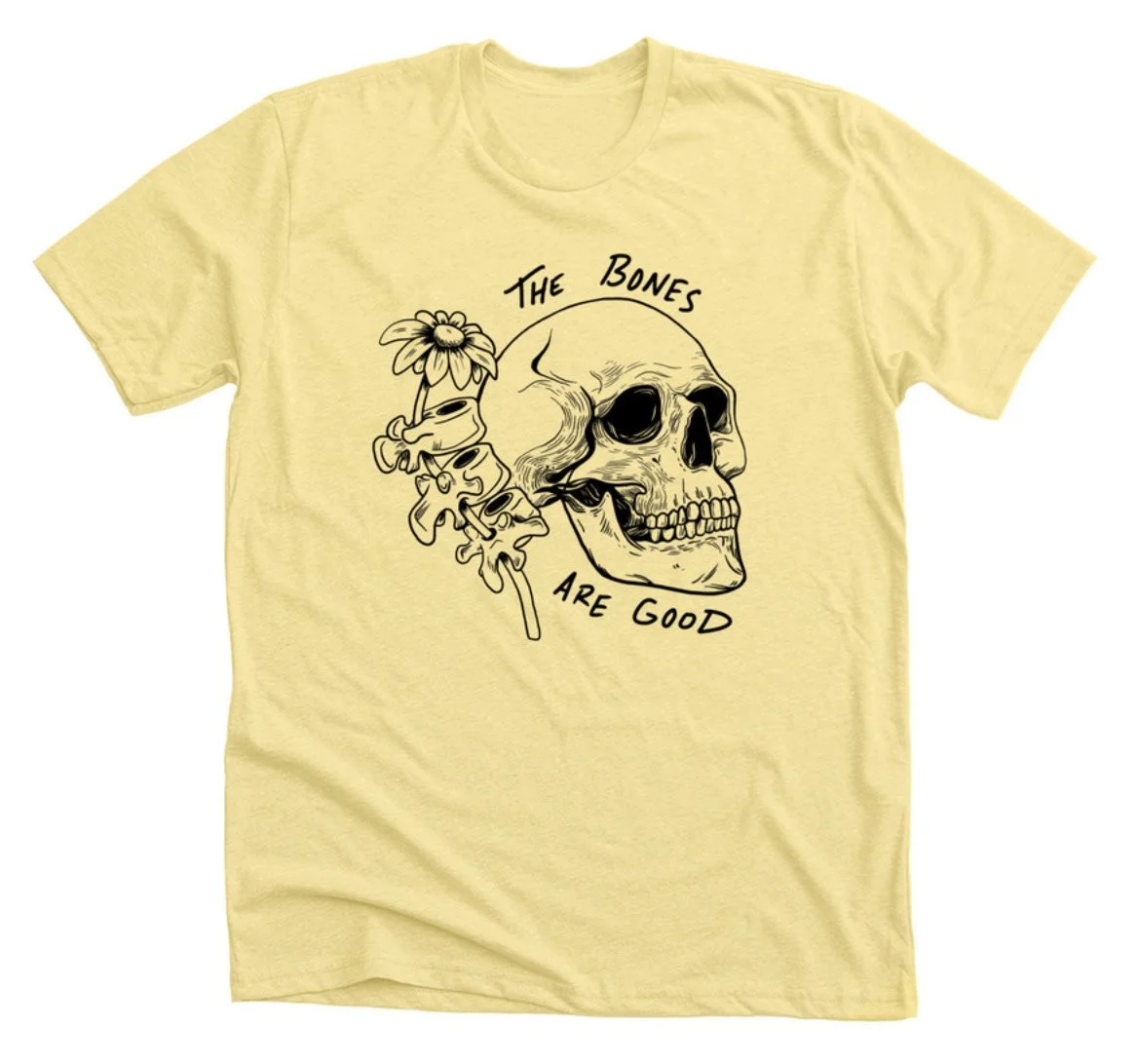 Yellow T-shirt with a black illustration of a skull and flowers. Text reads 'The Bones Are Good'.