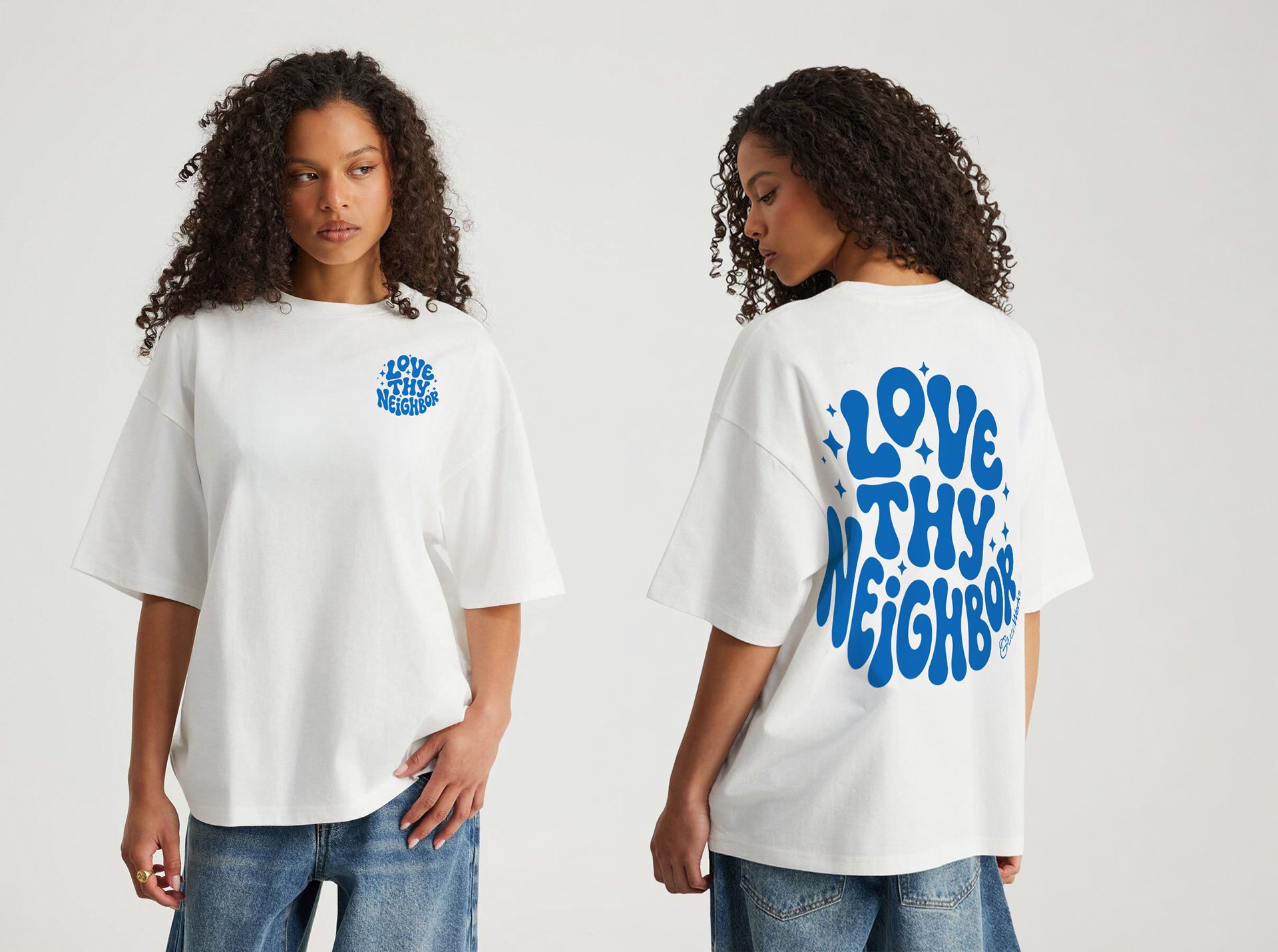 Two women wearing oversized white T-shirts with blue text and graphics, standing against a plain background. One woman faces forward with a small printed message on the front, while the other shows the message on the back in large, bold blue text.