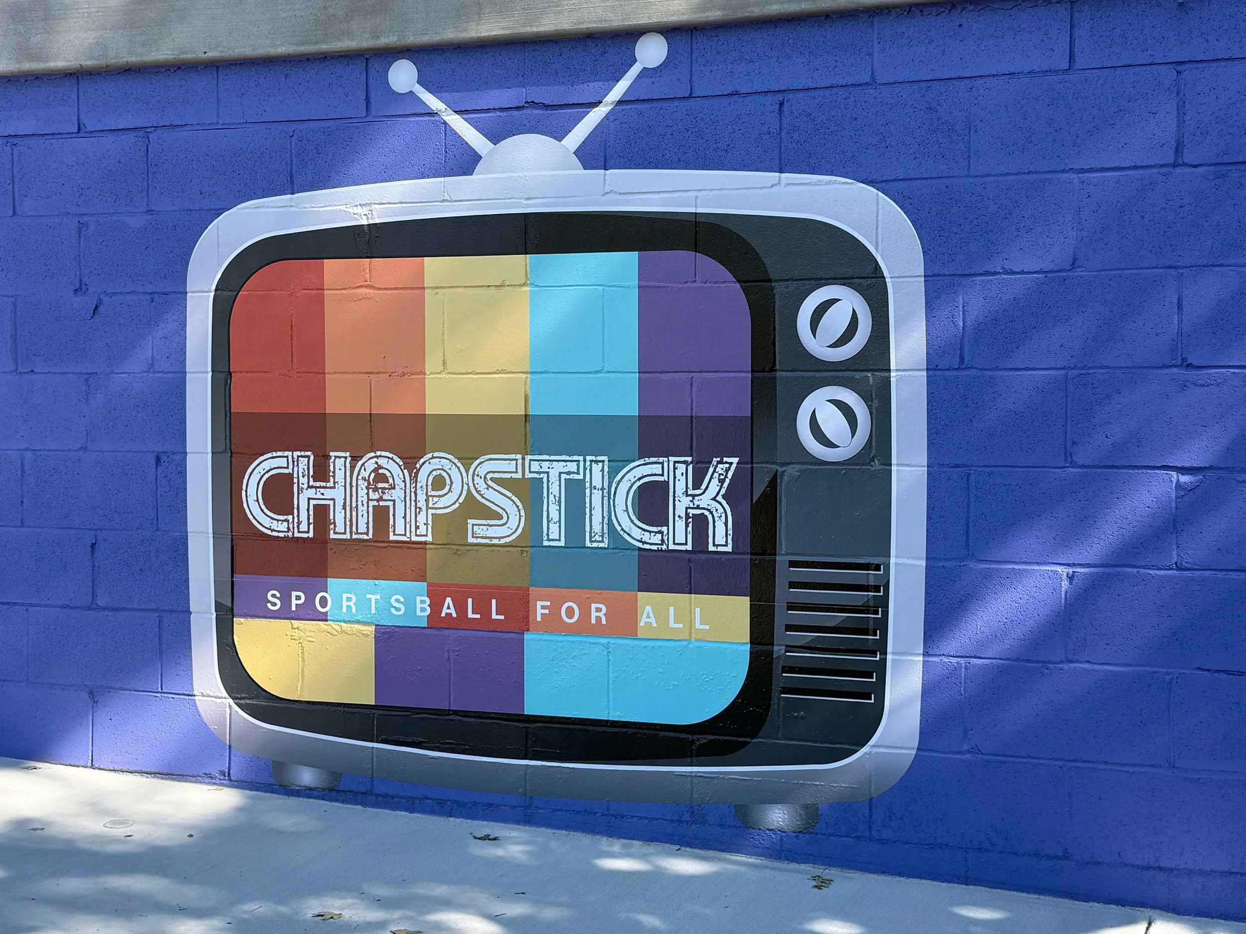 Colorful mural of an old-fashioned television with a rainbow test pattern on the screen, and the words 'ChapsTick' and 'Sportsball for All' painted on it.