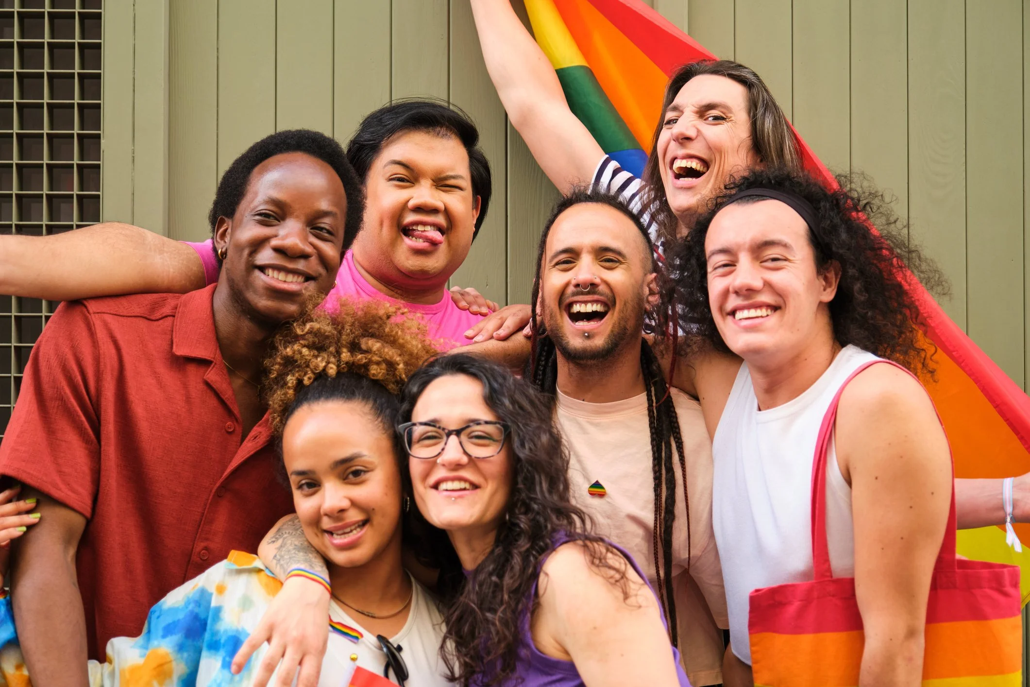 On MyMindset NYC Counseling Services website a diverse group of LGBTQIA+ people smiling and posing together in front of a rainbow flag.