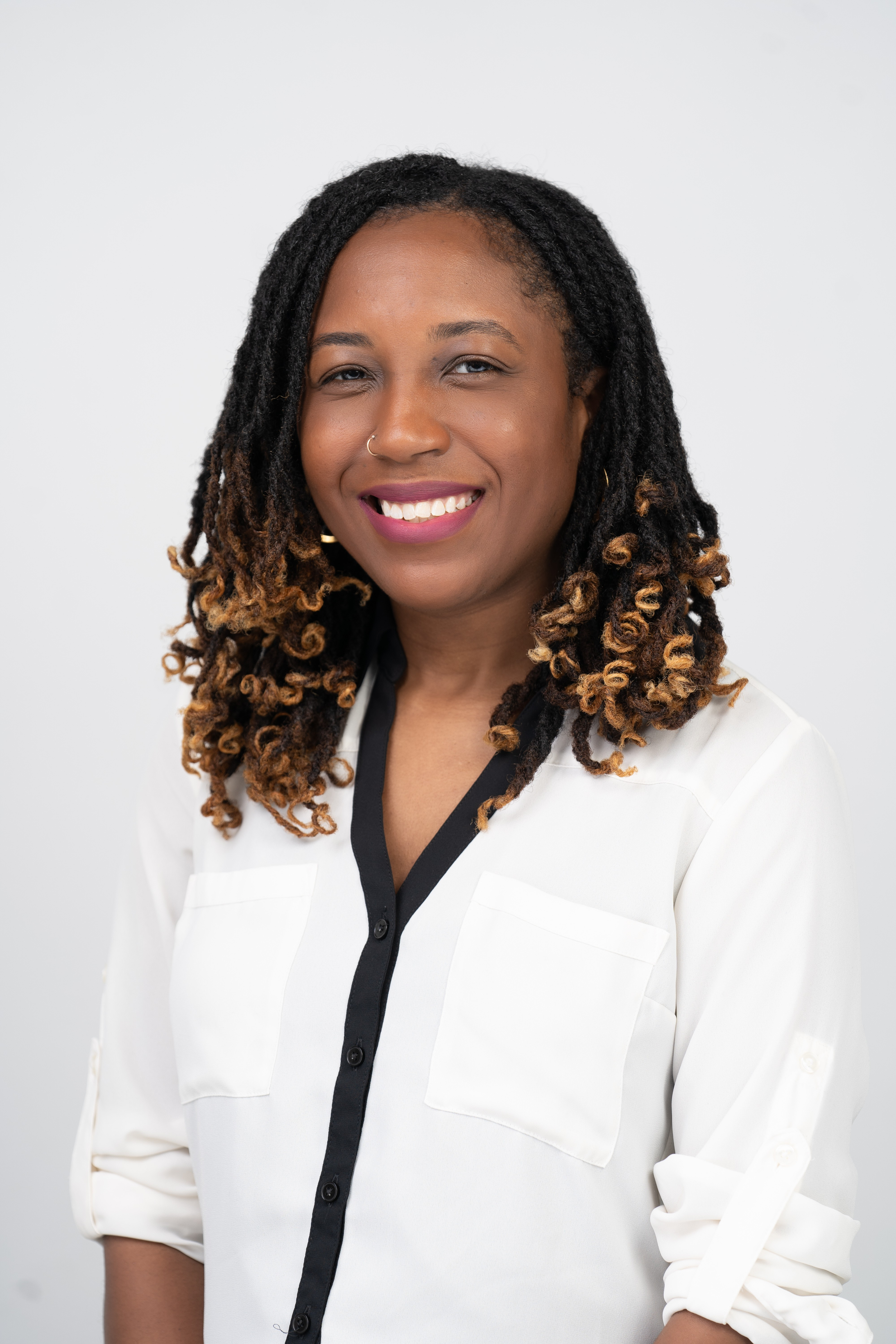 Portrait of Jessica Thomas lgbt therapist African American woman with long microlocs, smiling, wearing a white blouse with black trim, against a plain white background. Portrait of owner of MyMindset.