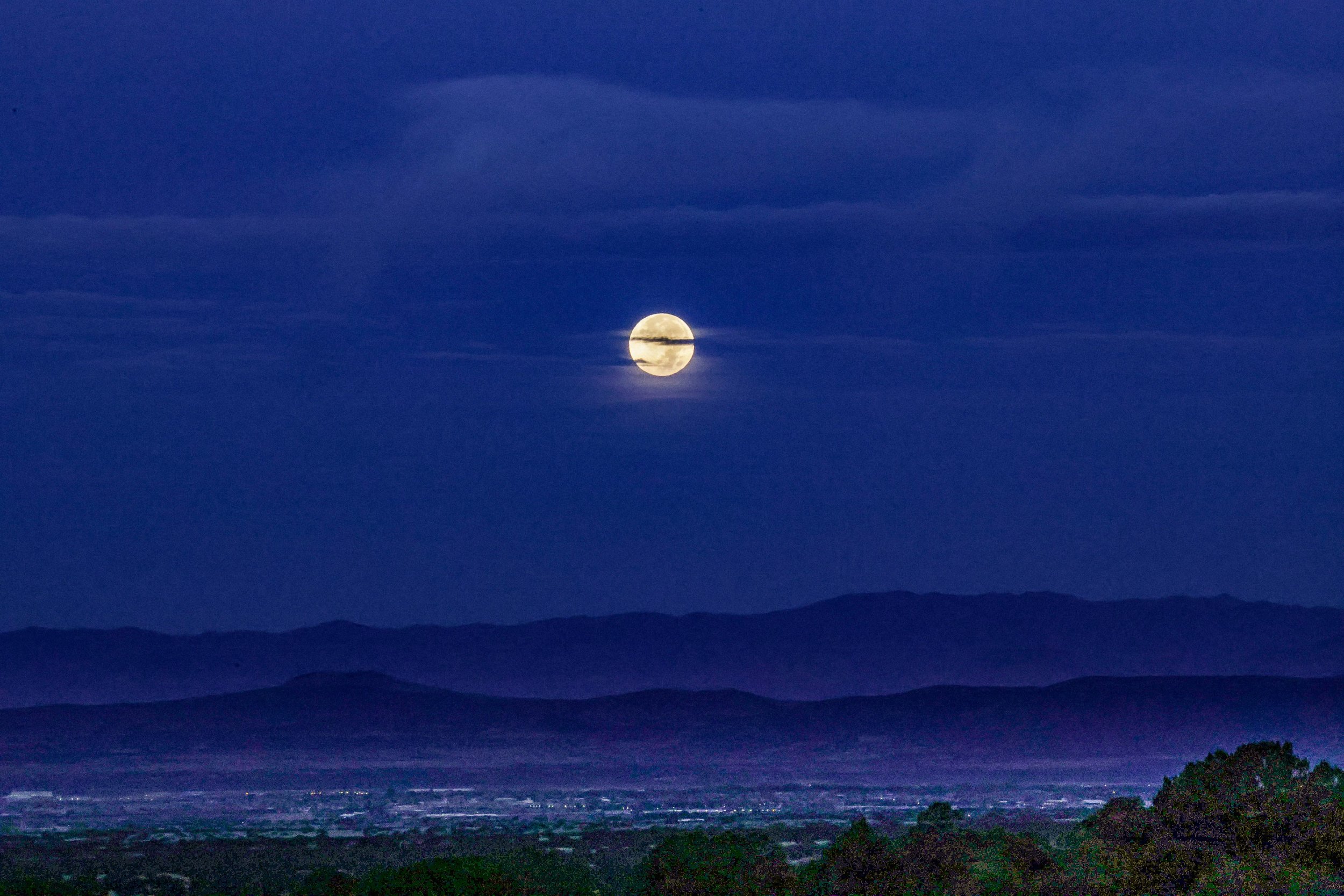 Full moon over a nighttime landscape with clouds and distant hills