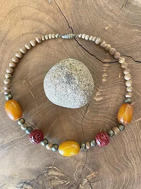 Beaded necklace with large amber and red beads, surrounding a round stone, on wooden background.