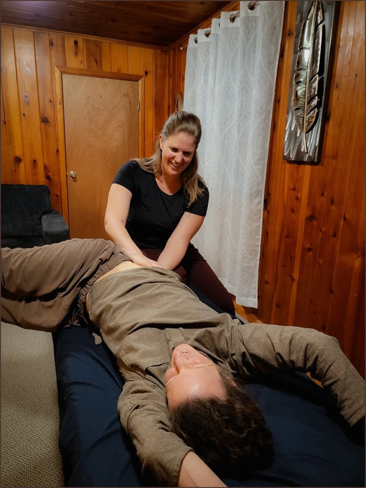 A woman giving a massage to a man lying on a massage table in a wooden-paneled room.