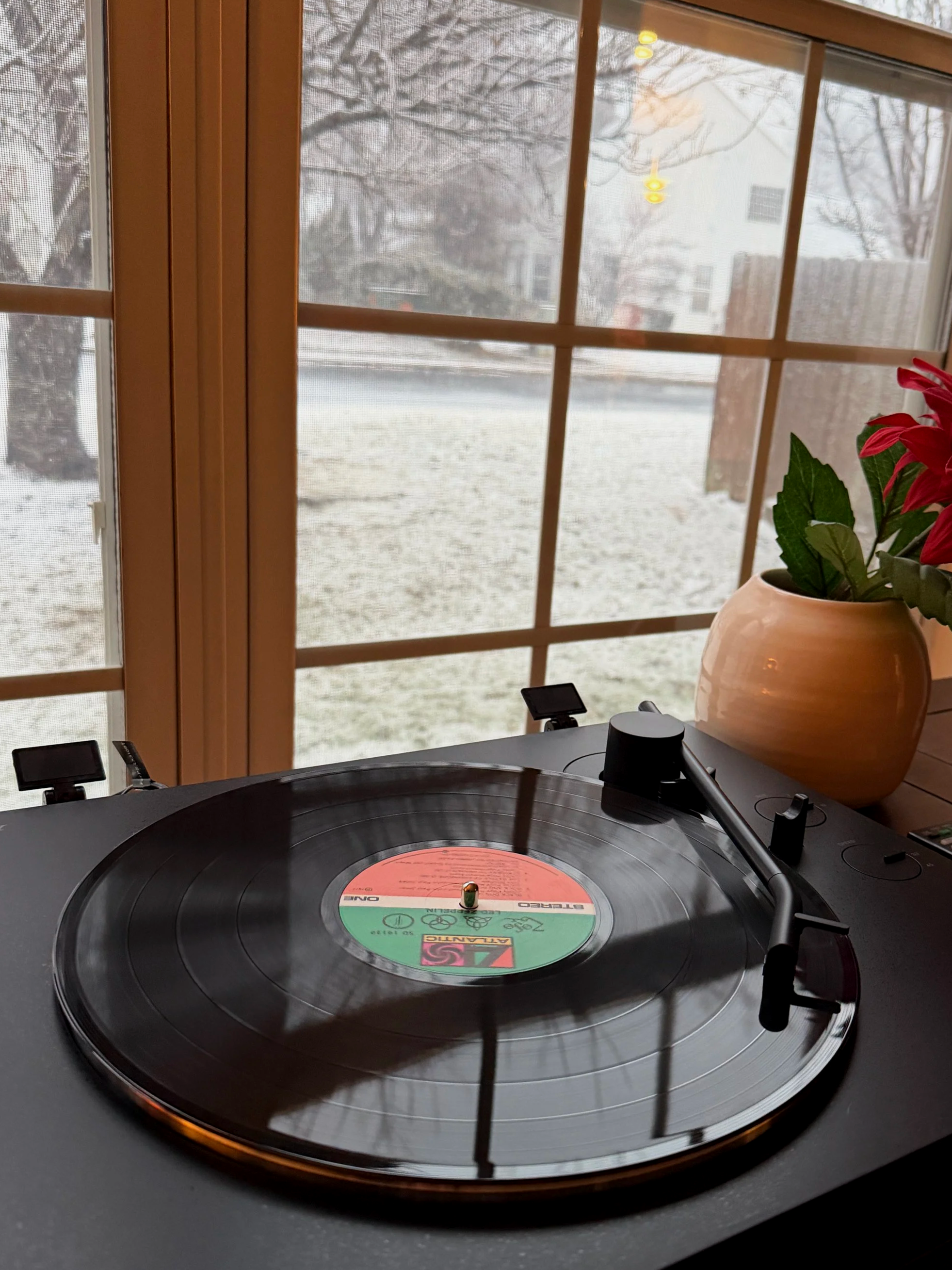 Vinyl record spinning on a turntable by a window as snow falls outside on a winter day