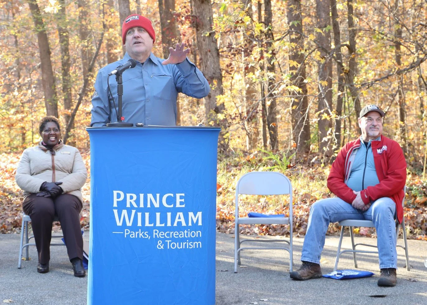 Martin Fernandez speaking at the Locust Shade Mountain Bike Trail ribbon cutting ceremony hosted by Prince William County Parks, Recreation & Tourism, with MORE President Ernest Rodriguez and Supervisor Andrea Bailey seated behind him.
