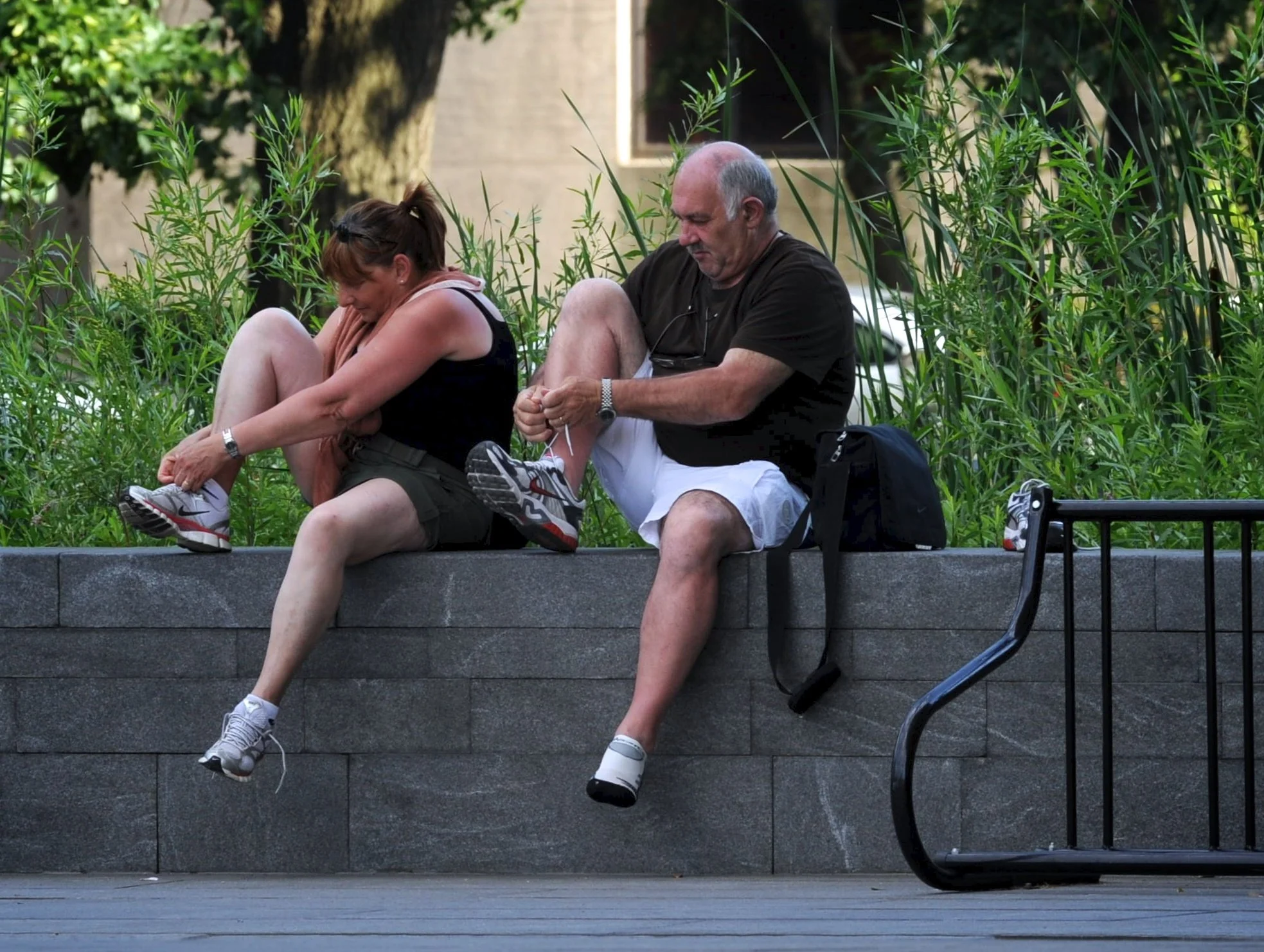 A couple adjusts their shoes while sitting on a retaining wall outside a museum