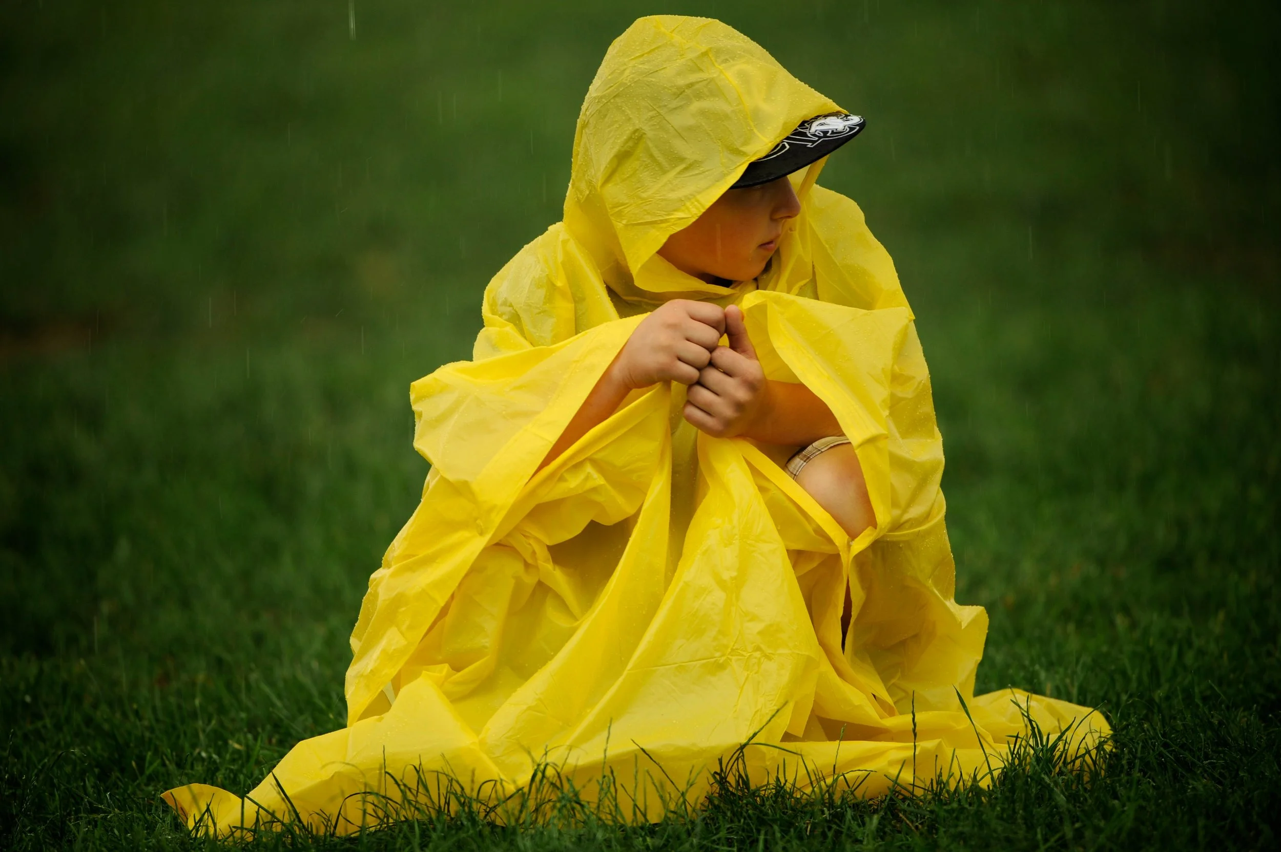 A young boy huddles under a poncho during a brief summer rain at the National Mall