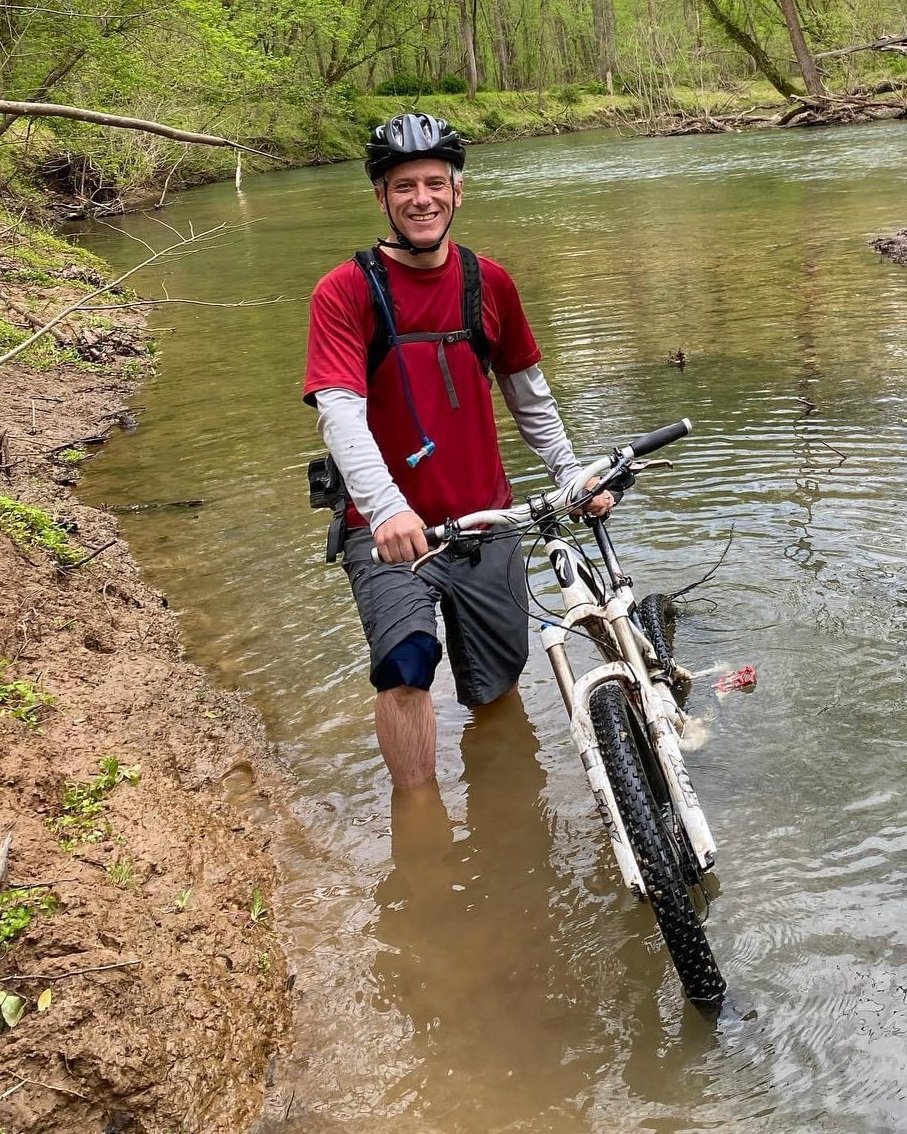 Casey Anderson walking his bike across the Patapsco River.
