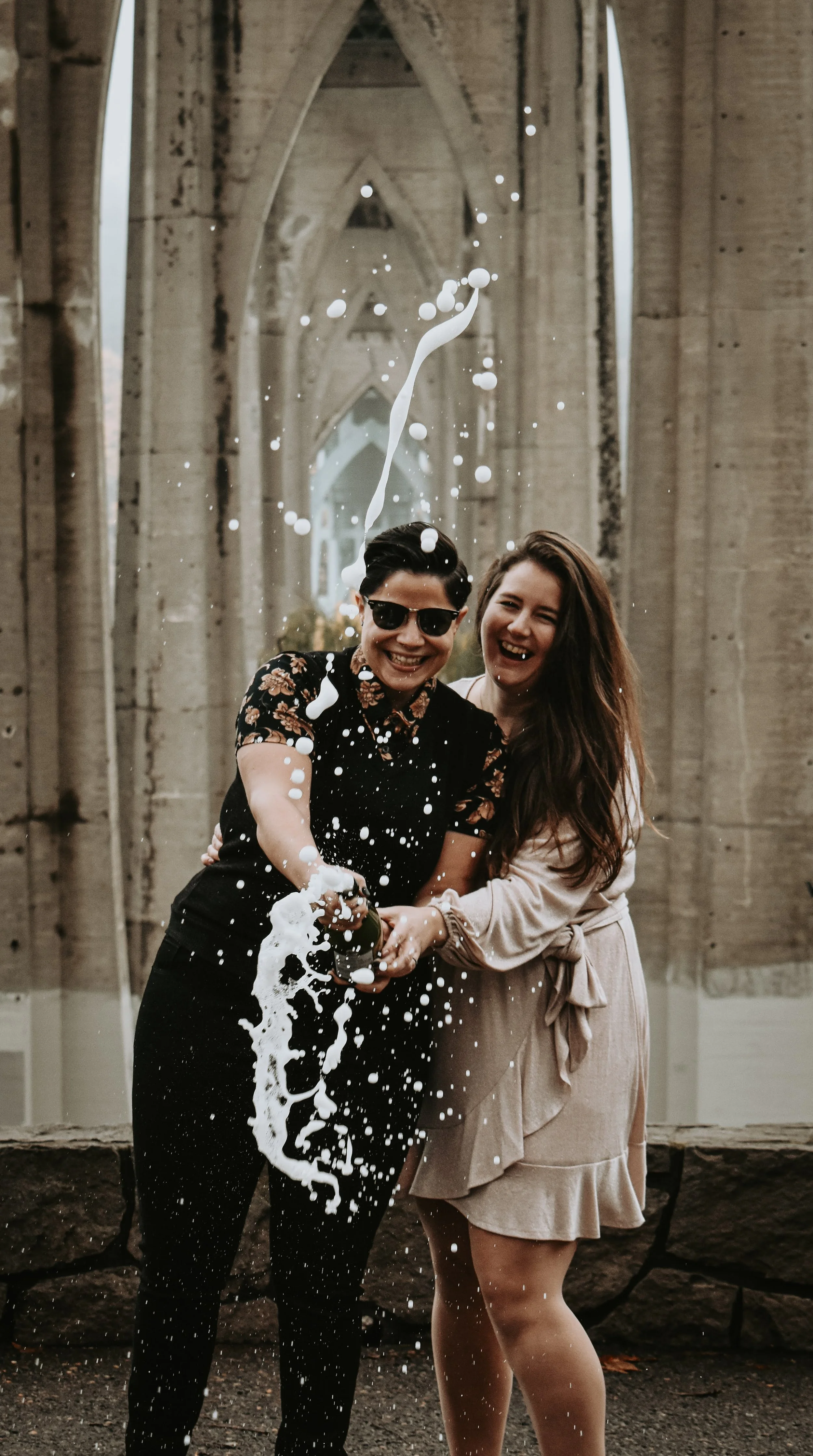Lesbian couple popping champagne under St. Mary's bridge a geometric bridge in Portland Oregon