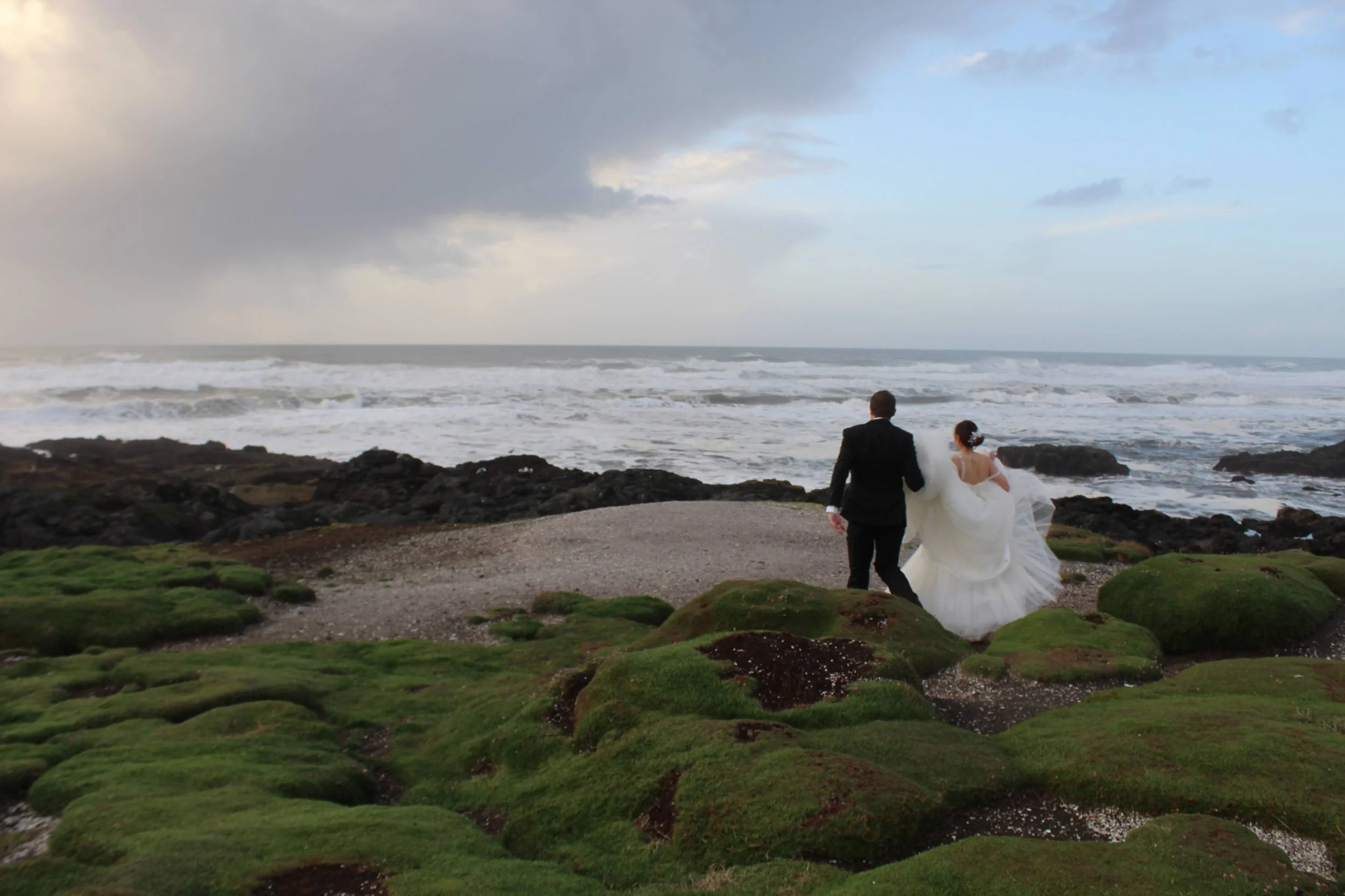 A bride and groom running towards the ocean on a cliff in oregon