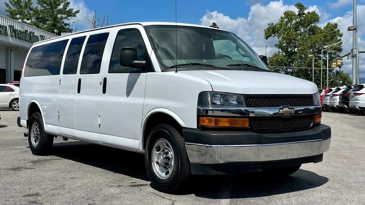 A white Chevrolet cargo van parked in a lot with other vehicles, under a partly cloudy sky.