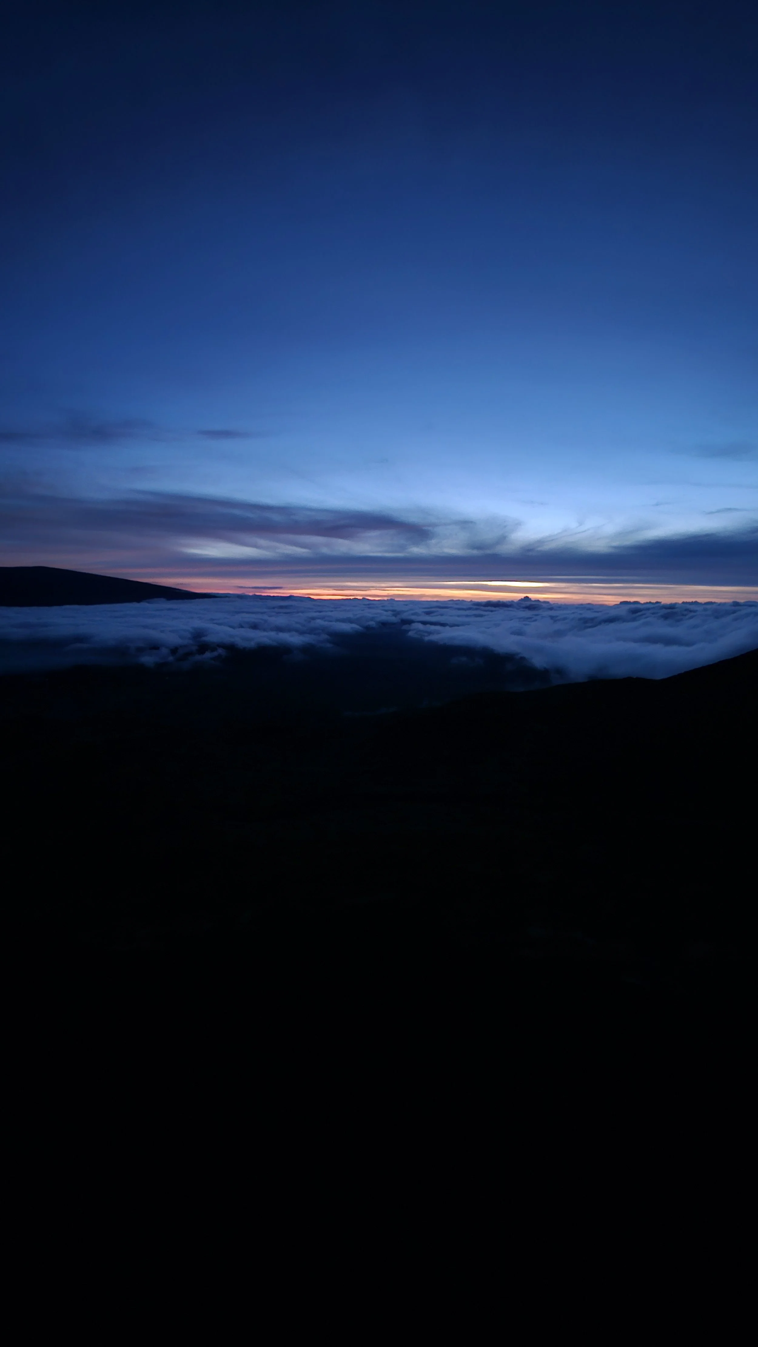 Two women singing into a microphone on stage with a colorful mural of a man playing drums in the background. There are audience members in the foreground.