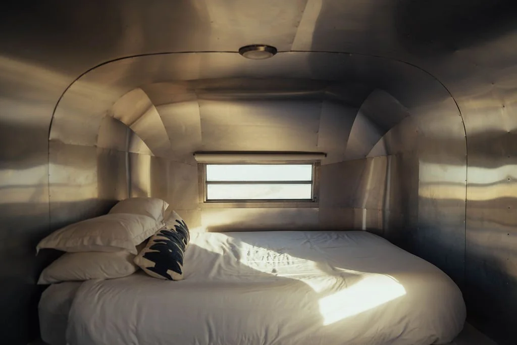 Interior of a small, metallic, camper van with a bed, pillows, and a window.
