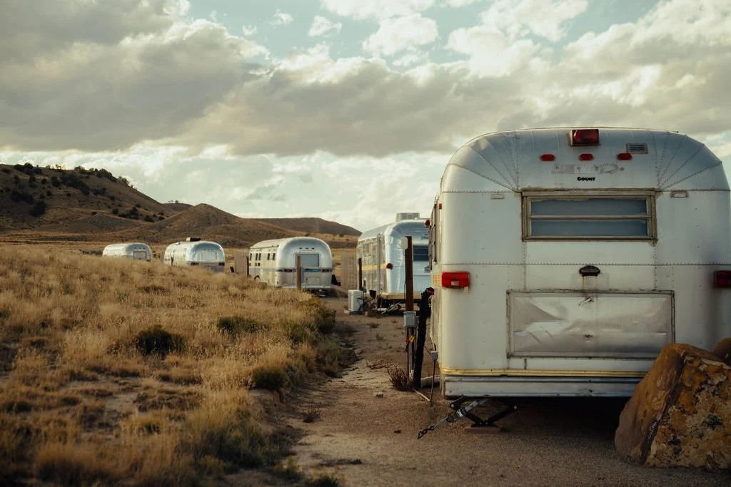 Multiple RVs parked in an open scenic field with hills in the background and cloudy sky overhead.