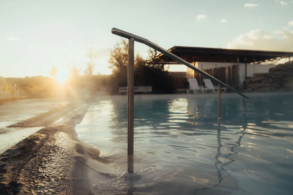 A swimming pool during sunset with a metal handrail and lounge chairs in the background.