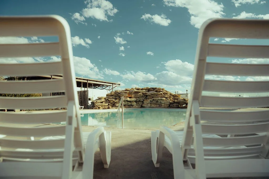 Close-up of a water fountain splashing in a swimming pool during sunset, with a cloudy sky and a wooden fence in the background.