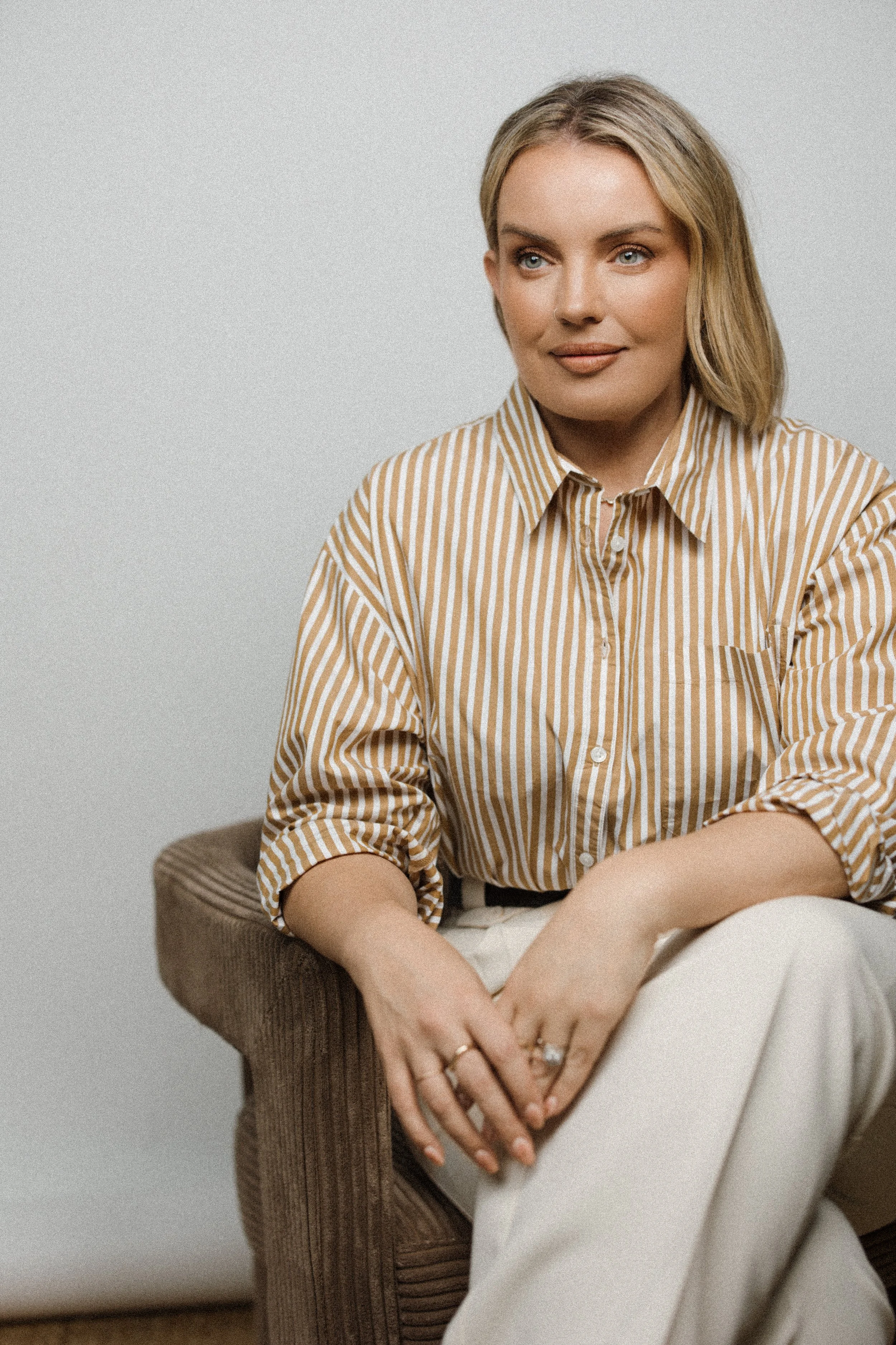 A photograph of a blonde woman sitting with her legs crossed looking out to the side