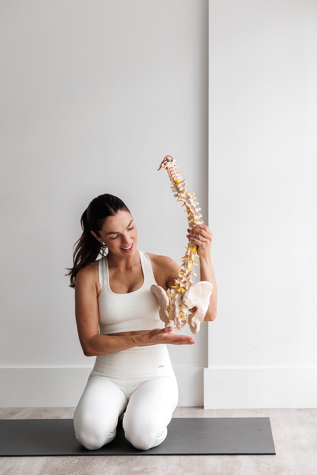 The Mama Physio holding a pelvis and wearing white workout gear