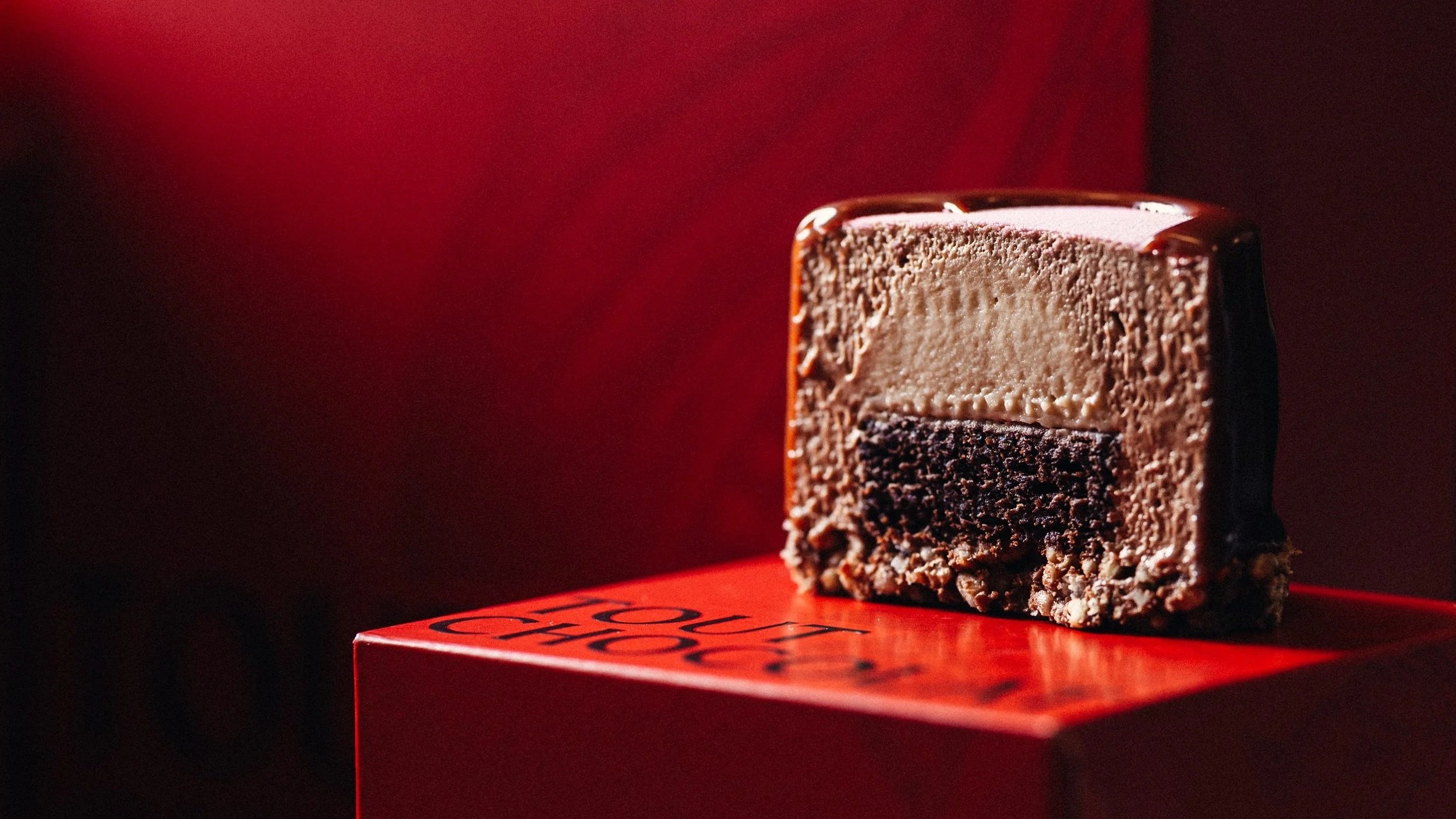 Gâteau au chocolat en coupe, avec une couche de chocolat sombre en bas et une couche de mousse de chocolat plus claire en haut, placé sur un support rouge.