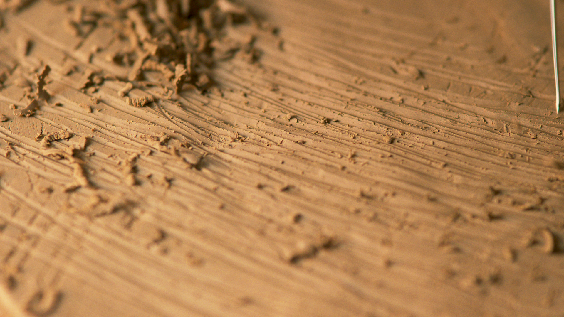 A close-up of a chisel cutting into wood, creating shavings and textured lines in a Multi-Gyn commercial
