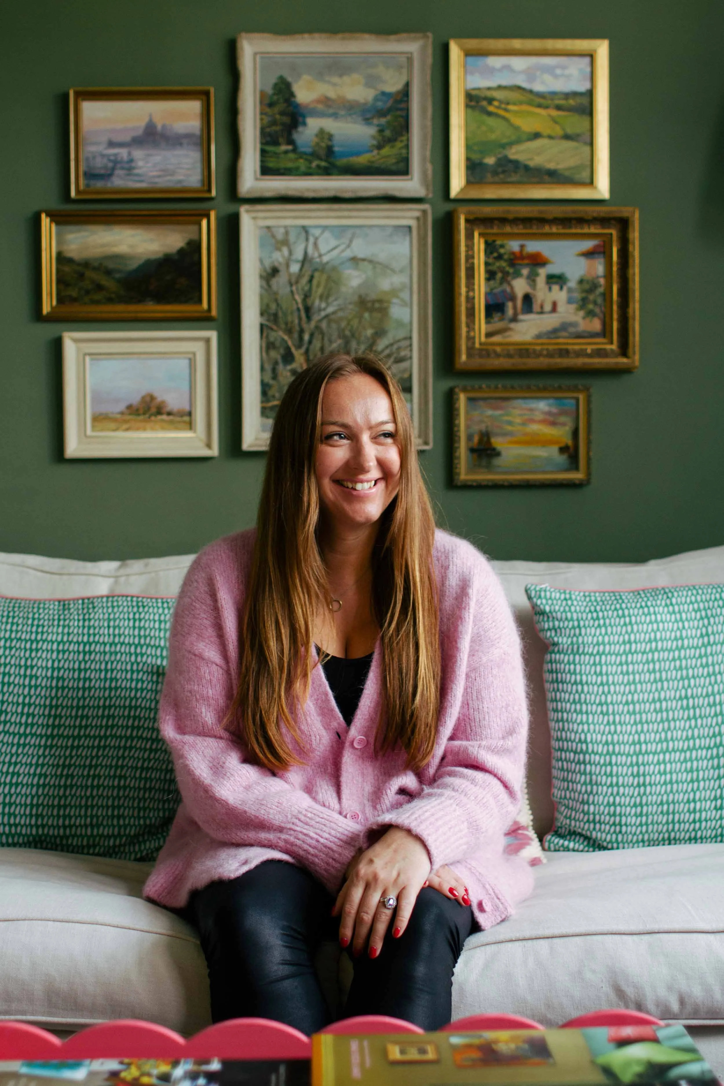Smiling woman sitting on sofa with paintings on wall behind her, brand portrait