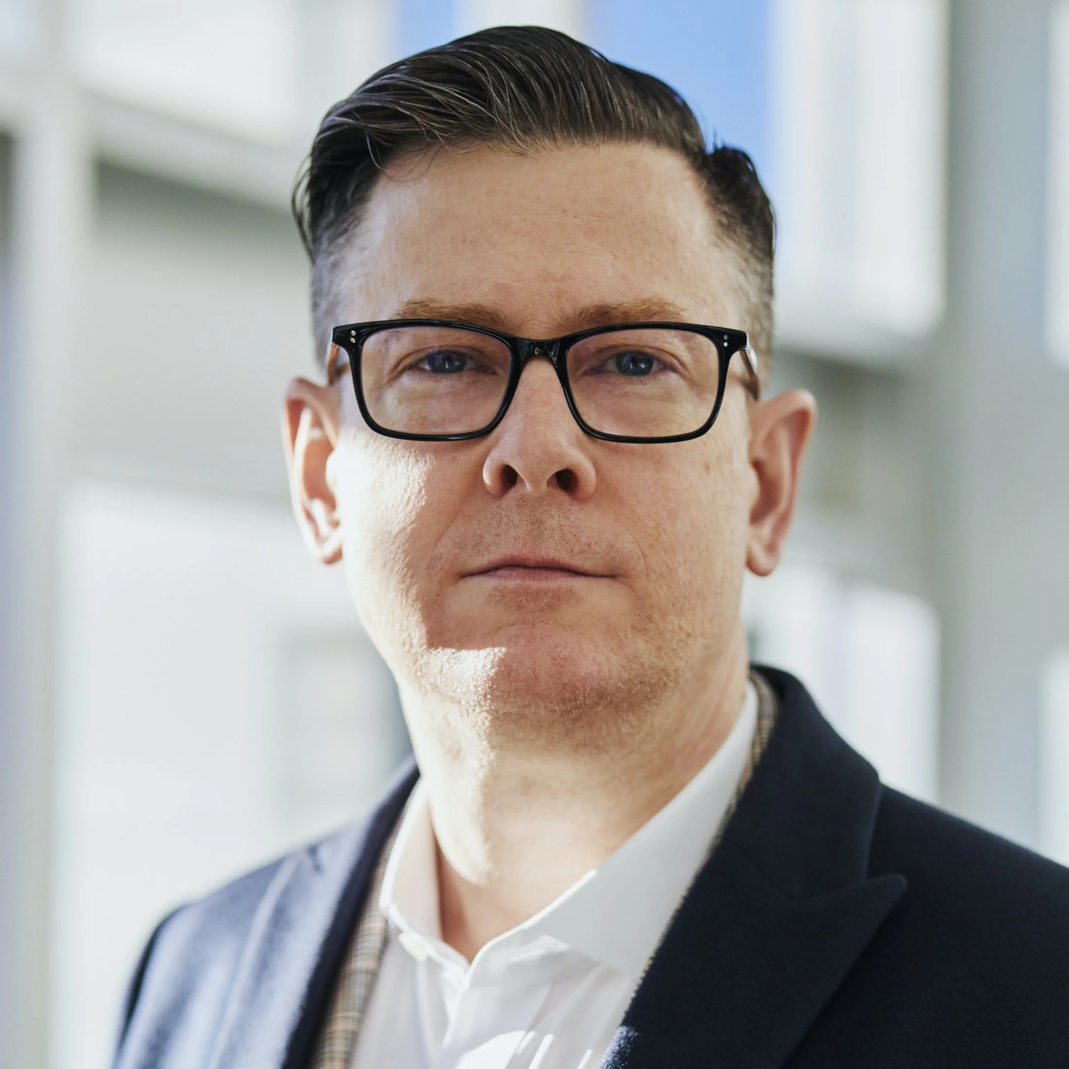 A man wearing glasses in an office setting, looking directly at the camera.