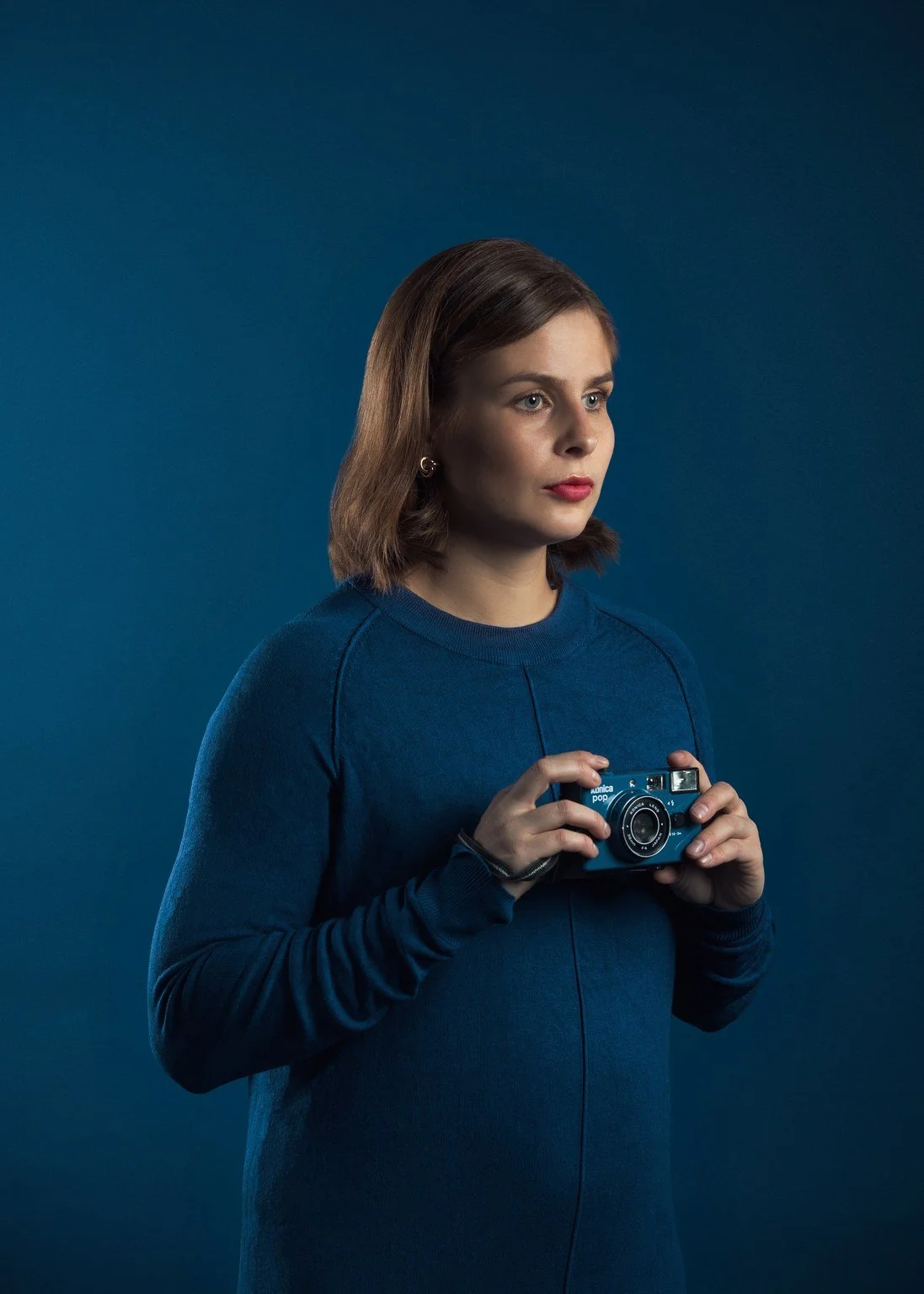 Nuori nainen, jolla on ruskea lyhyt tukka, pitää mustavalkoista kameraa käsissään, taustalla sininen väri.