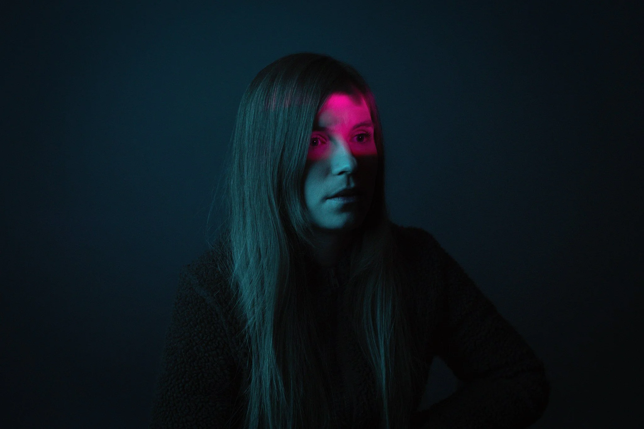 Vihreä- ja pinkkivaloa heijastava hämäräkuva nuoresta naisesta, jolla pitkä, suora tummanruskea tukka, taustalla tumma tausta.