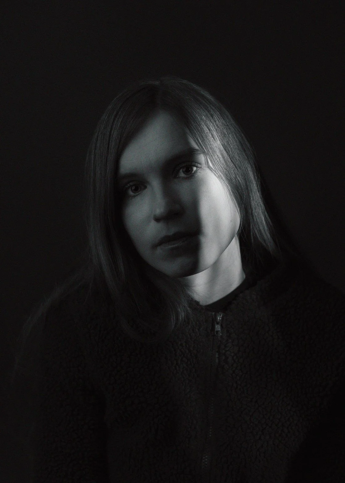 Mustavalkoinen kuva nuoresta naisesta, katse suoraan kameraan, tausta musta.