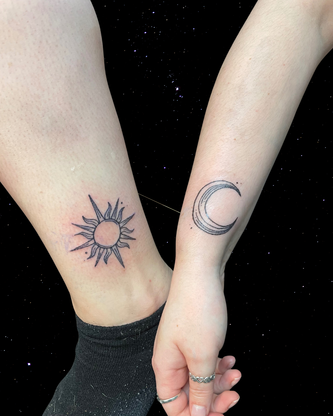 Two arms with Hand Poked Tattoo of a sun and a moo