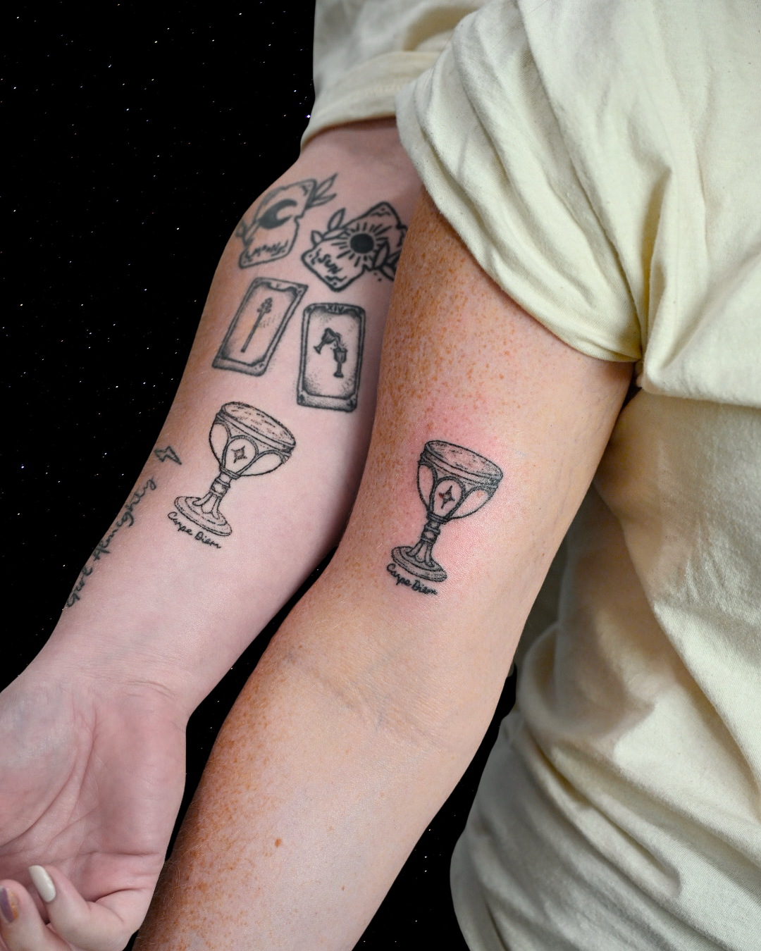 Two arms with matching hand poke tattoos of a chalice with the text "carpe diem" below
