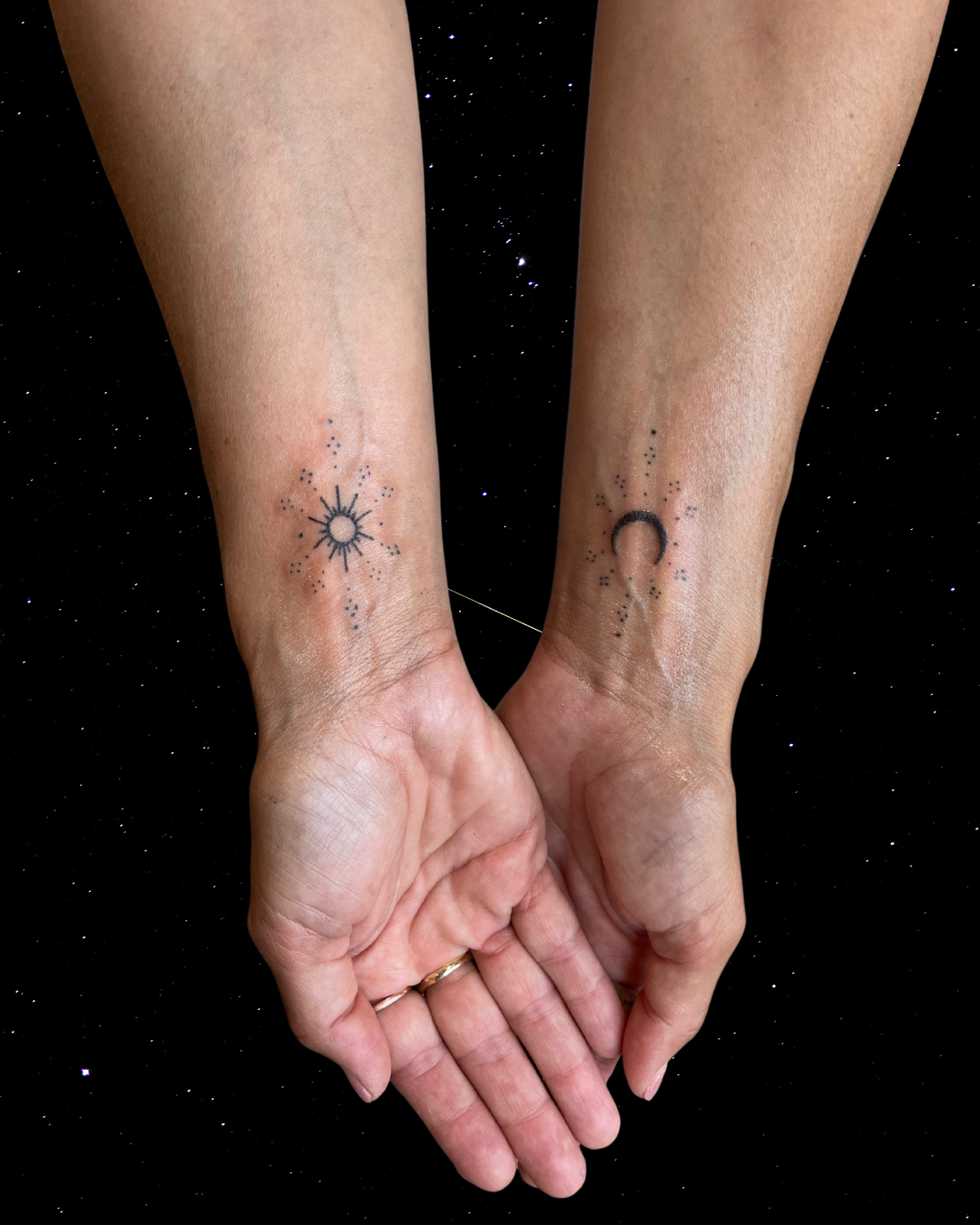 Hand Poked Tattoo of a Sun and Moon ornament on someone's wrists