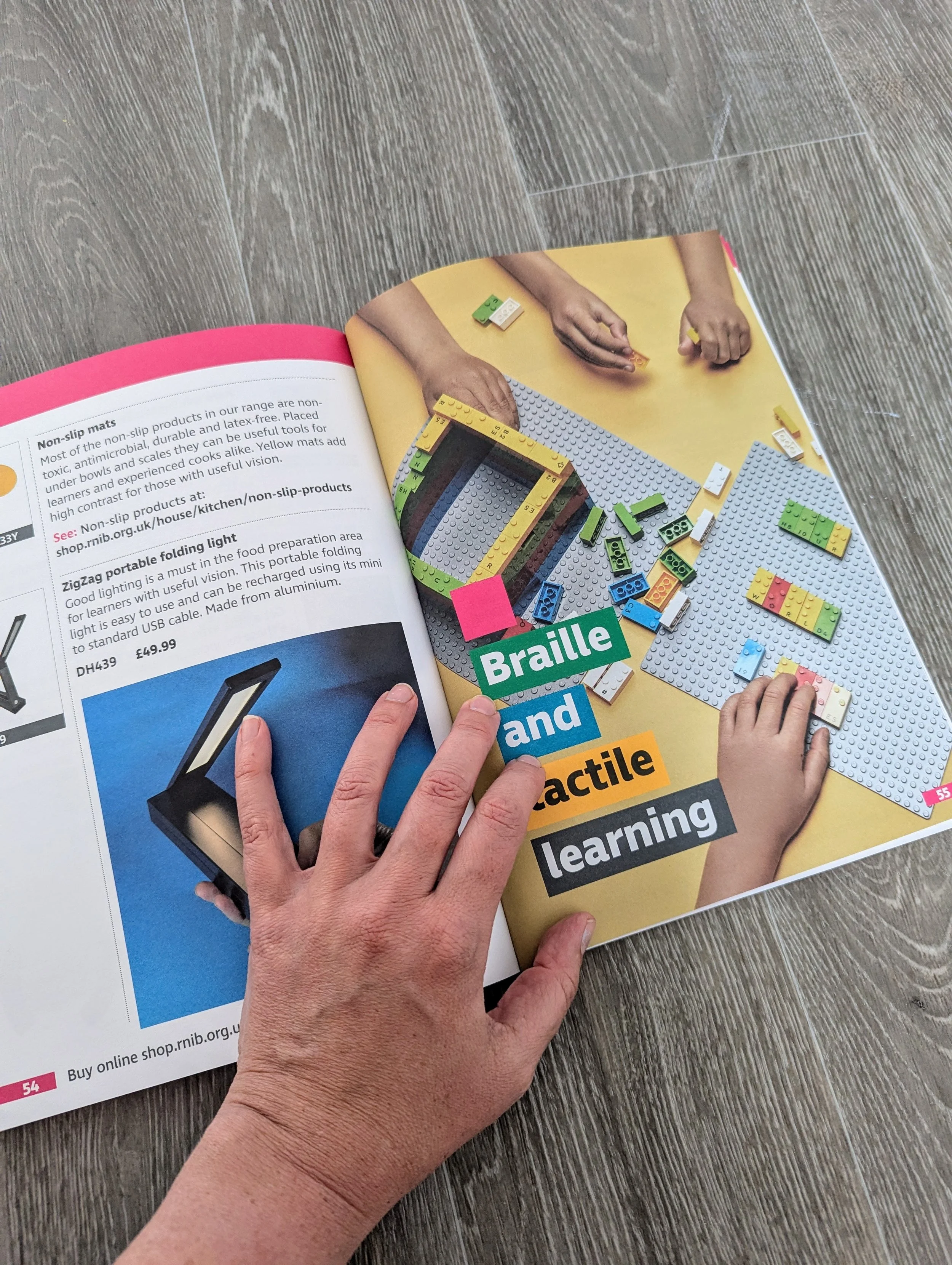 A person turning a page in a magazine with a colorful display of Lego bricks, a hand working on a Lego project, and the text 'Braille and tactile learning' on the page.