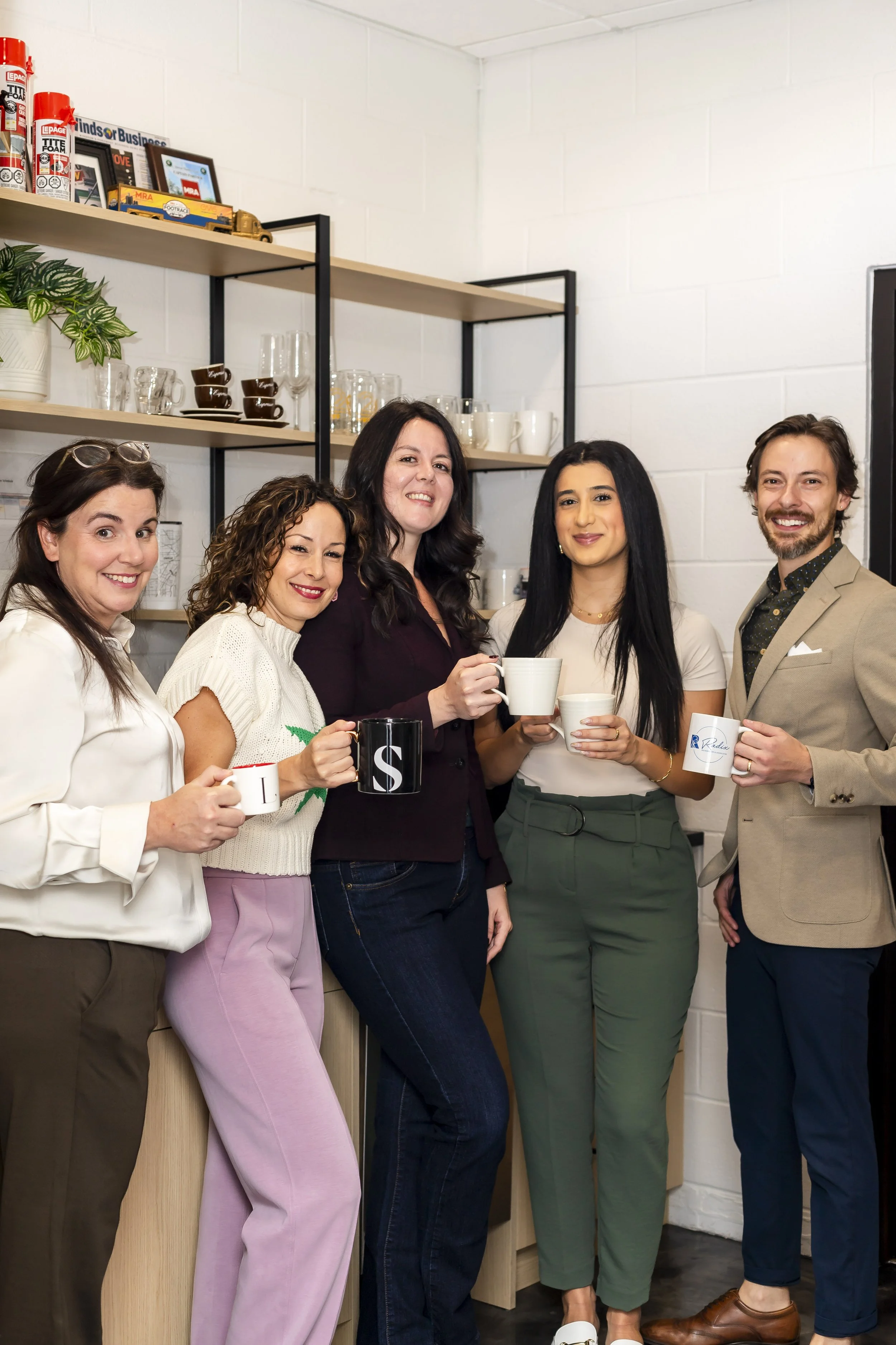 Five diverse people standing in a room, smiling, holding coffee mugs.